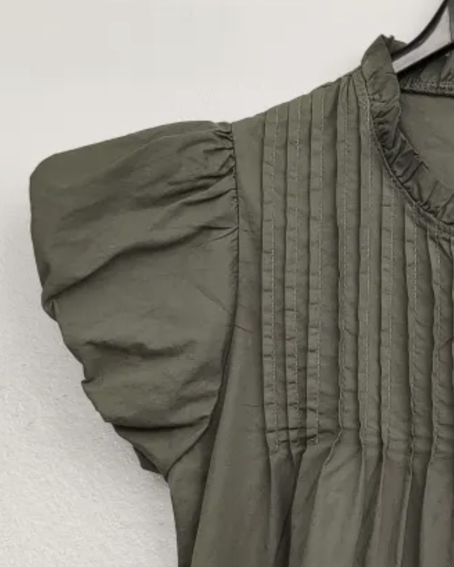Blusa verde com mangas franzidas e pregas verticais pendurada numa cabide