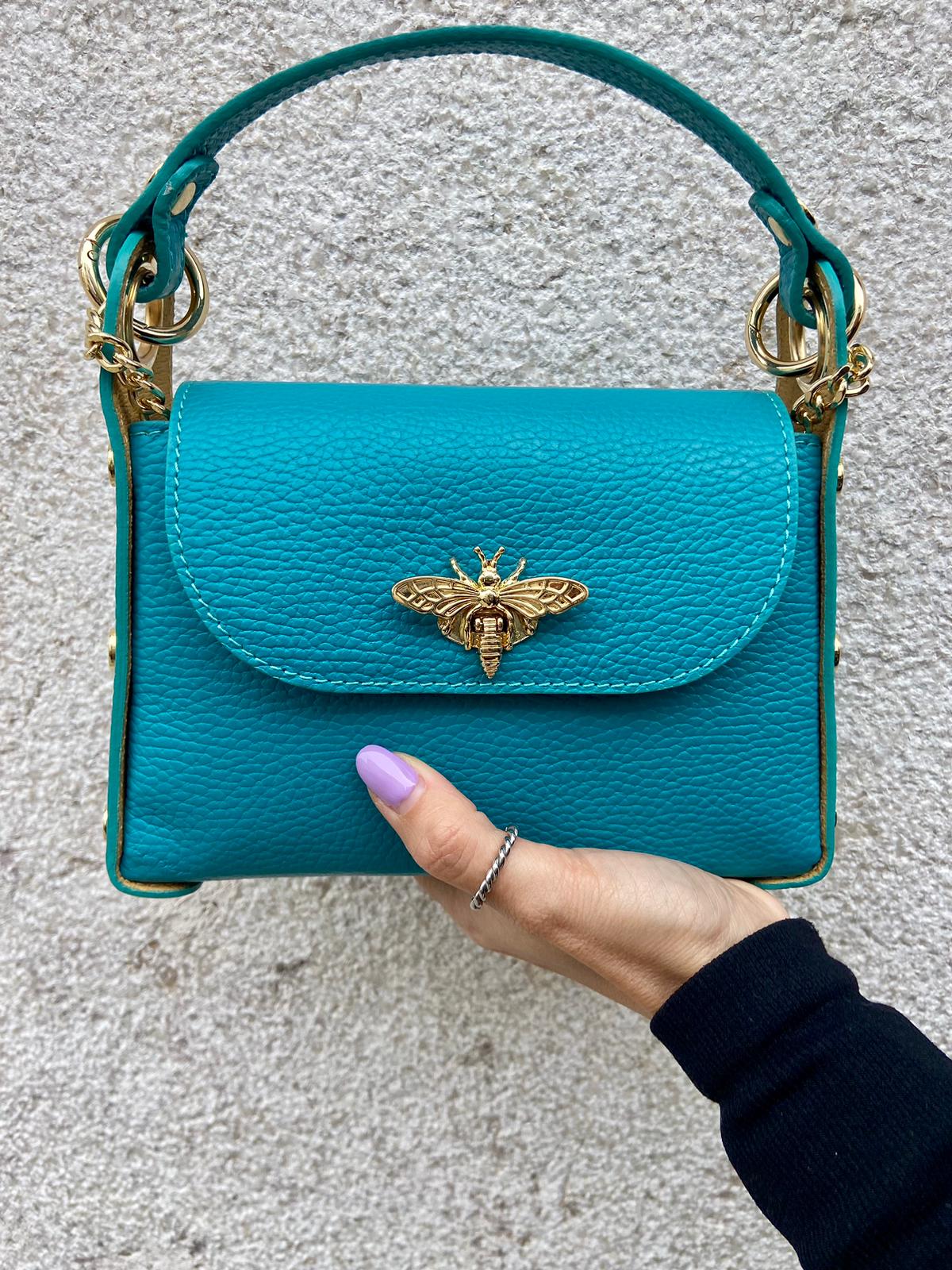 Mala pequena azul turquesa com adorno em forma de abelha dourada segurada por mão