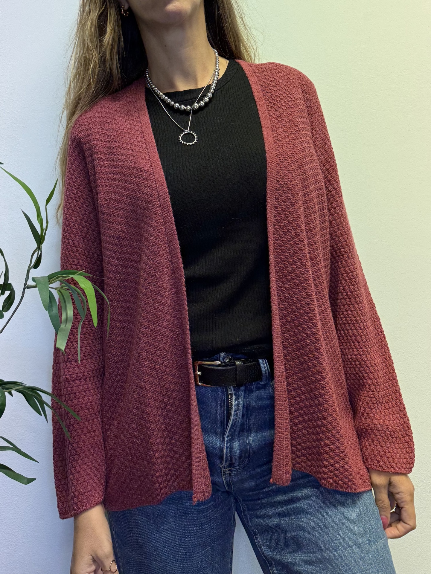 Mulher a vestir casaco de malha tijolo, camisola preta e calças de ganga azuis