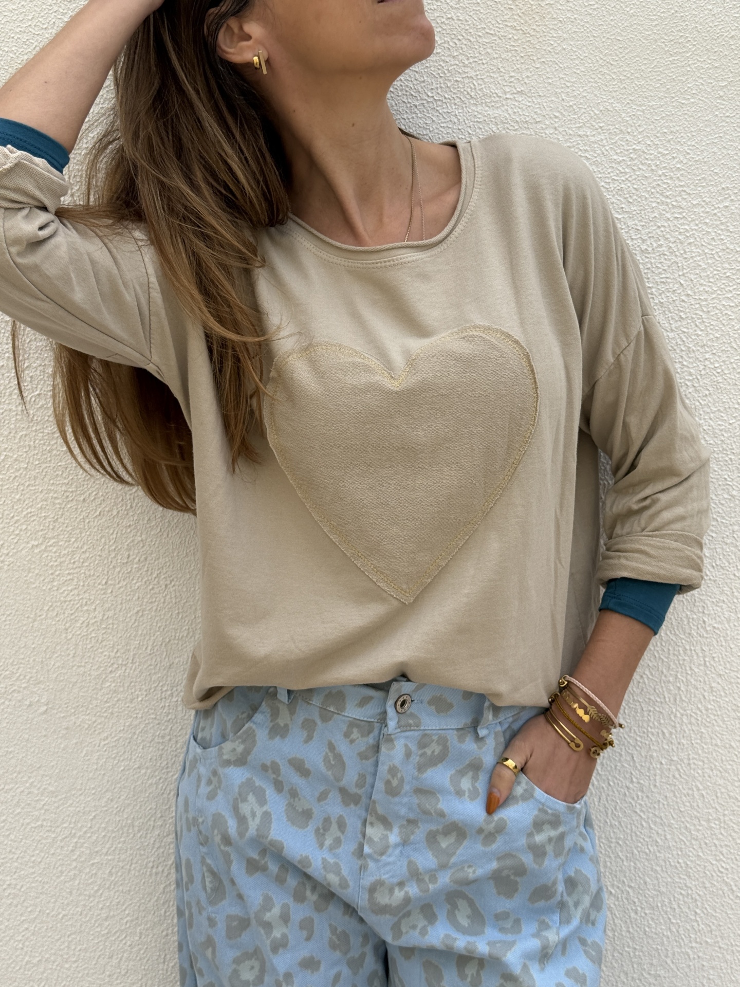 Pessoa com sweat bege com coração e calças azuis claras com padrão animal print cinzento