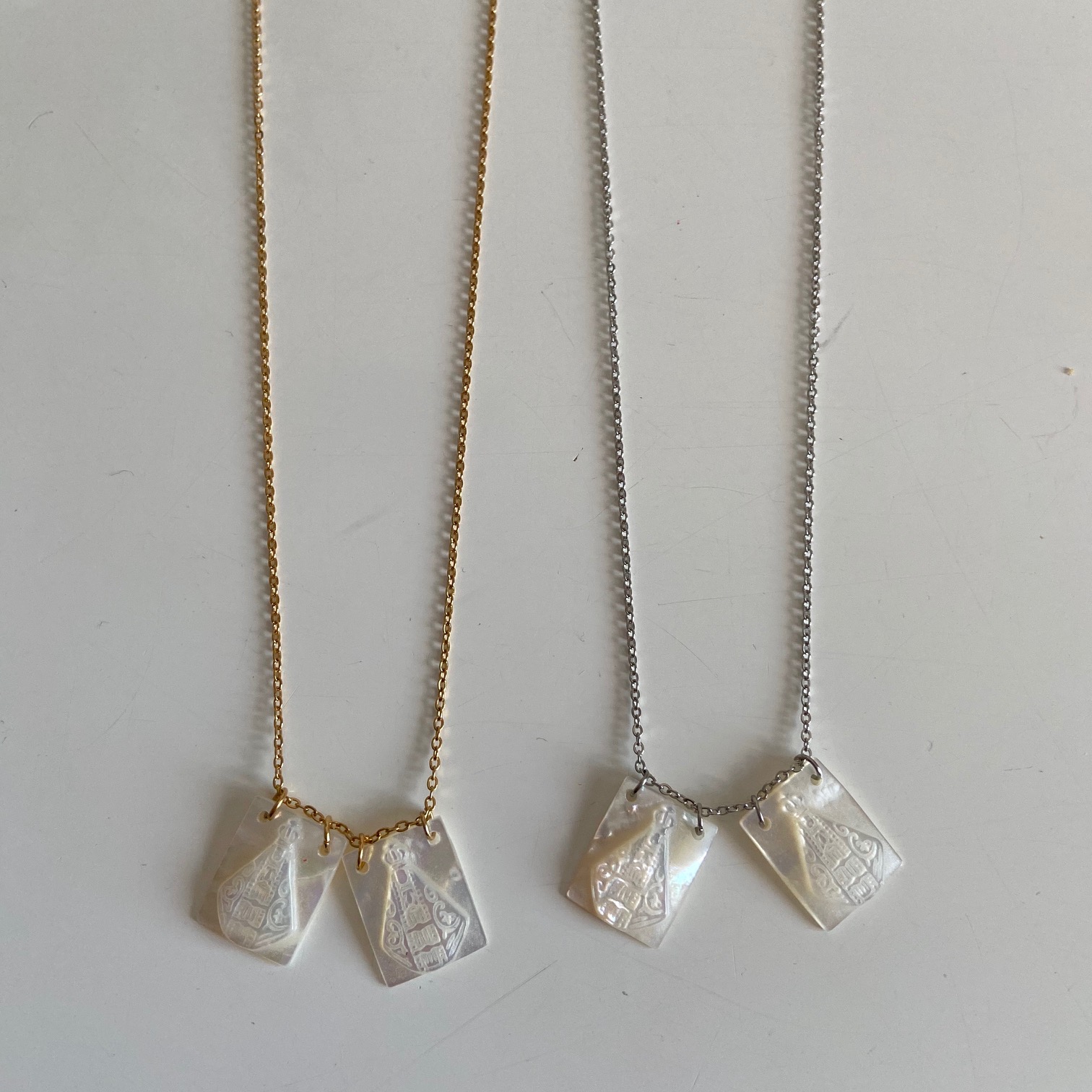 Dois colares com placas de madrepérola e correntes metálicas, dourado e prateado, sobre fundo branco.