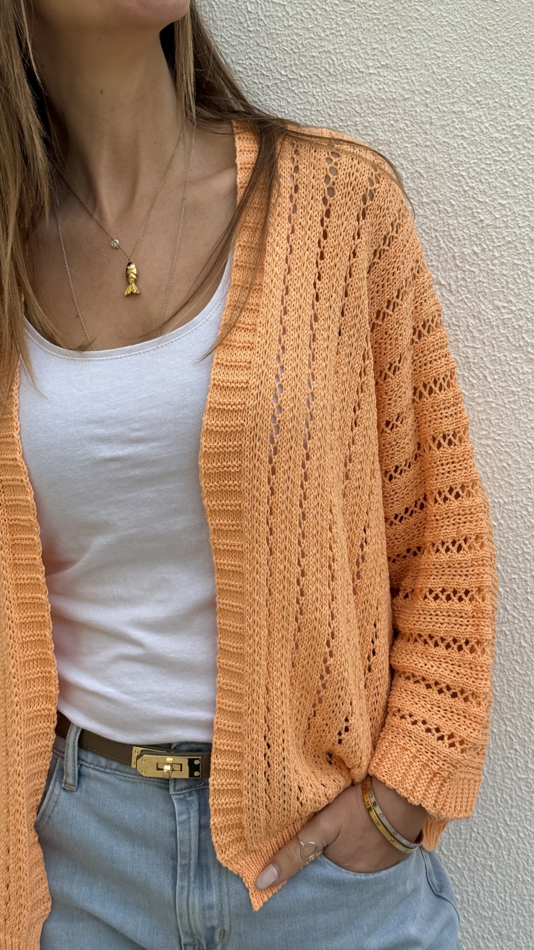 Cardigan laranja em malha com padrão de buracos usado com t-shirt branca e calças de ganga