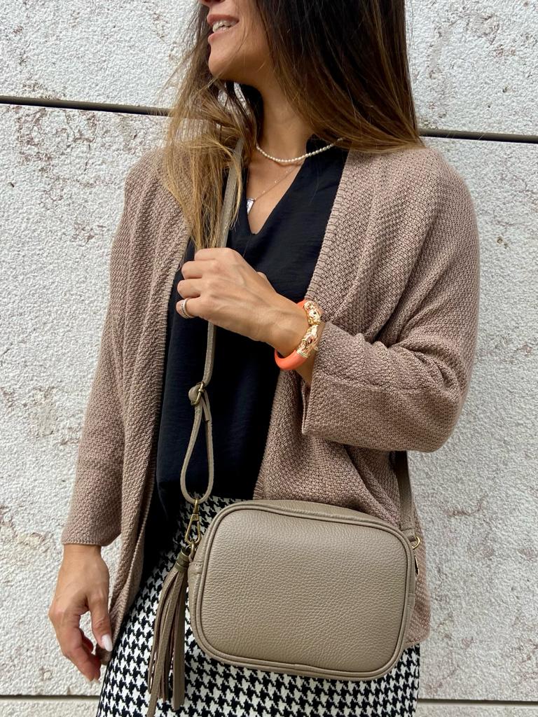 Mulher com cardigan bege, blusa preta, saia pied-de-poule, colar de pérolas, pulseira e mala bege de couro