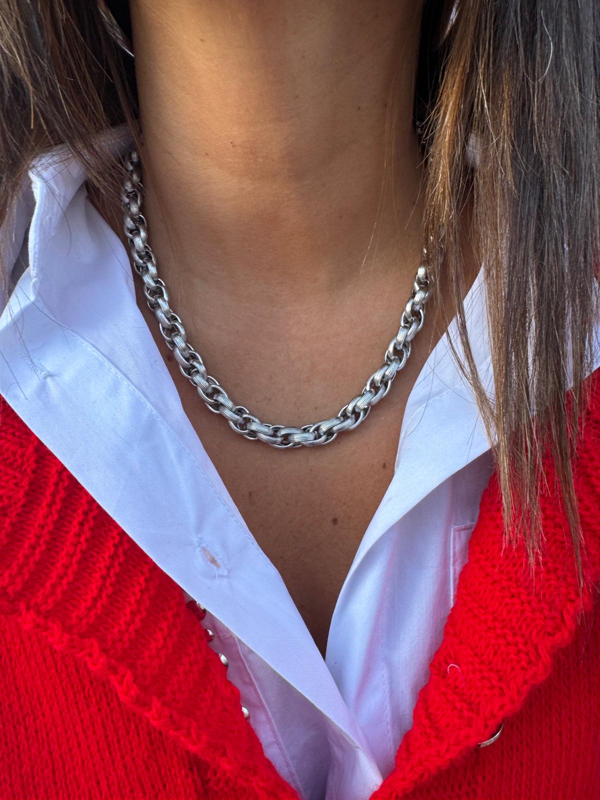 Colar de metal prateado com elos grossos, camisa branca e suéter vermelho tricotado.