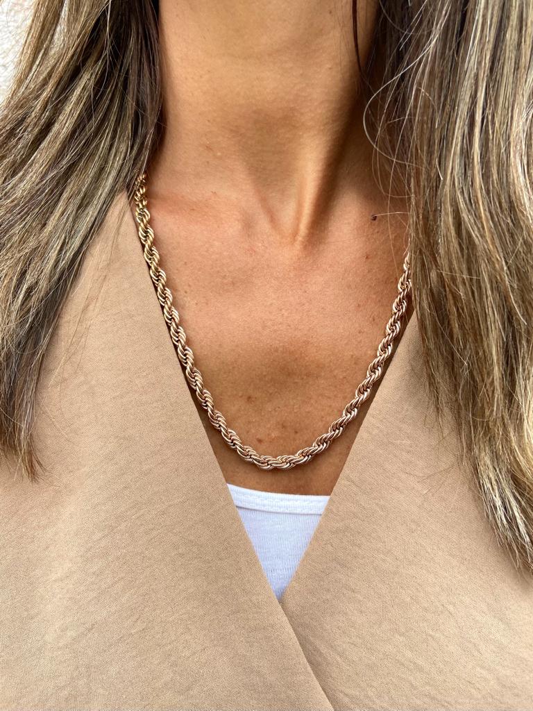 Colar dourado tipo corda em pescoço com casaco bege e camisa branca