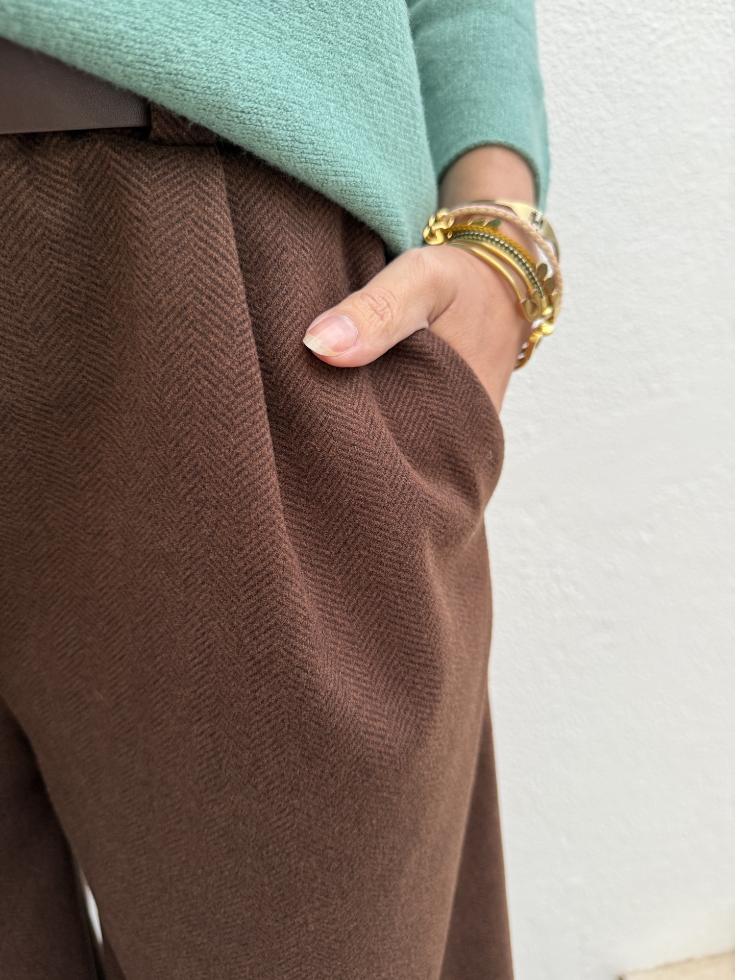 Calças castanhas padrão espinha de peixe e camisola verde claro com pulseiras no pulso