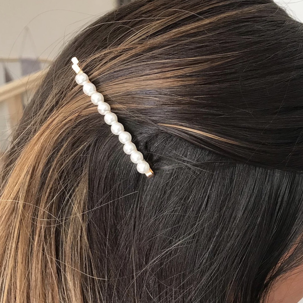 Presilha de cabelo dourada com pérolas num cabelo castanho com mechas claras