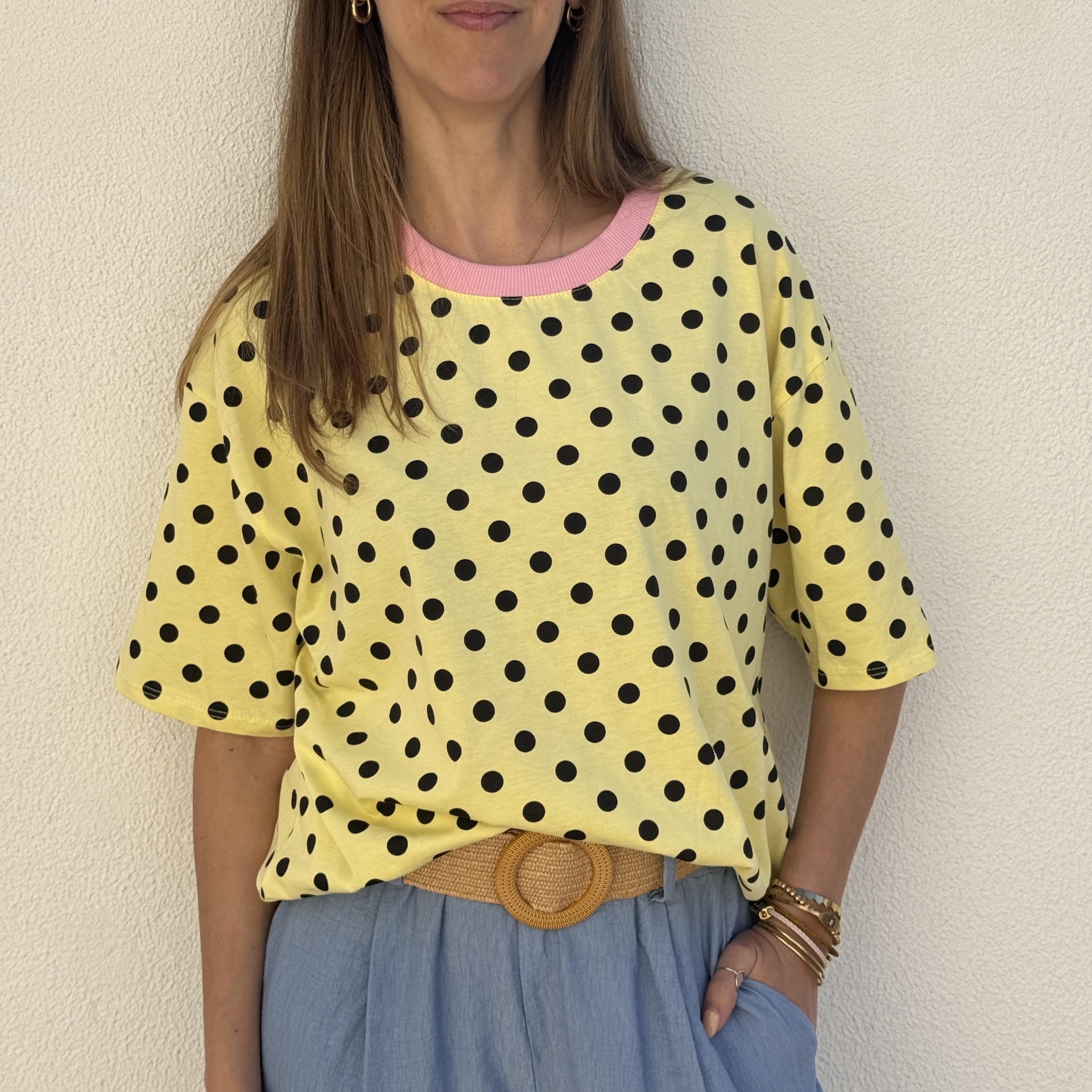 T-shirt amarela com bolinhas pretas e gola rosa, calças azul-claras e cinto castanho trançado.