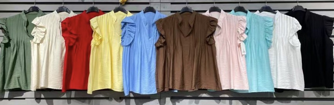 Dez blusas femininas de várias cores com mangas franzidas penduradas numa parede branca