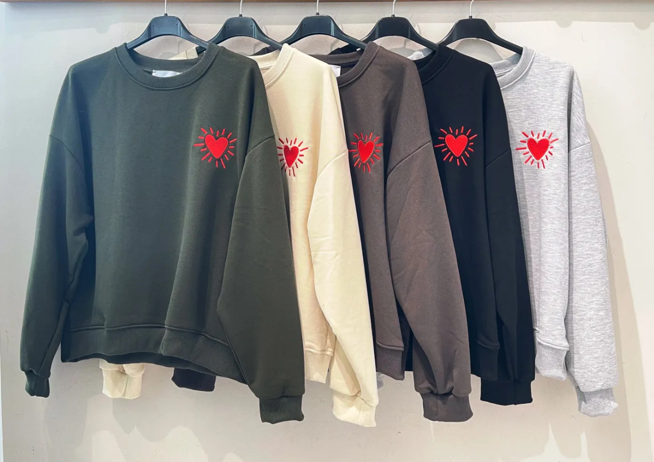 Cinco sweatshirts coloridas com bordado de coração vermelho penduradas