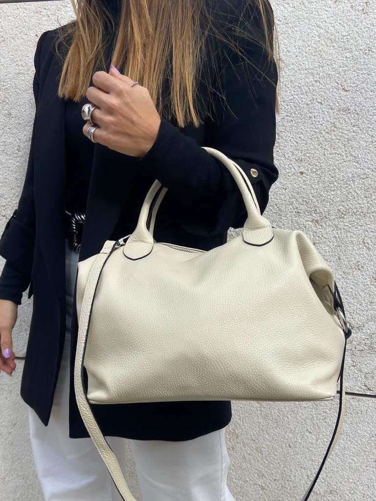 Bolsa creme em pele sintética com alça transversal junto a mulher com casaco preto