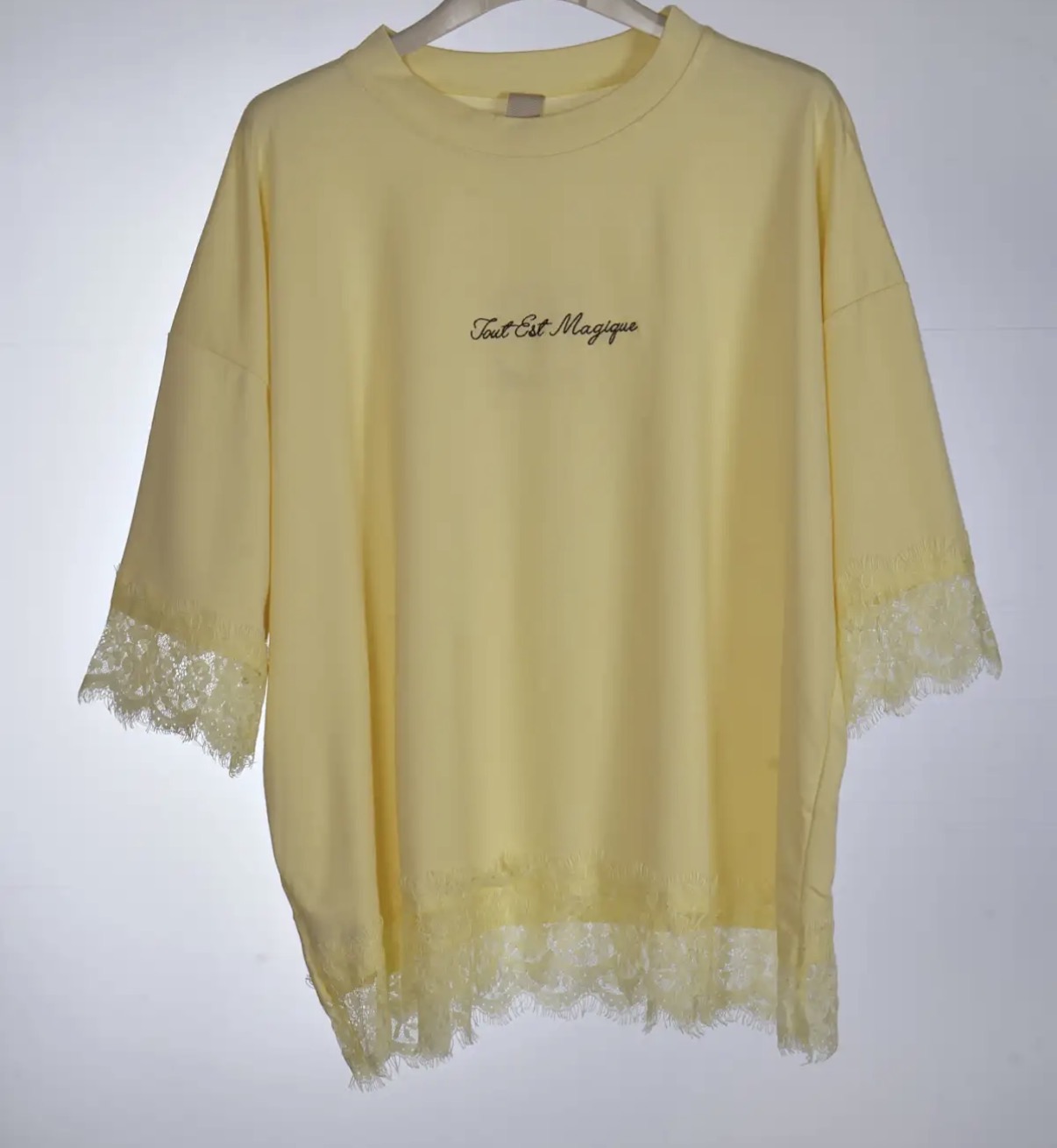 Camisola amarela com renda e texto bordado pendurada num cabide