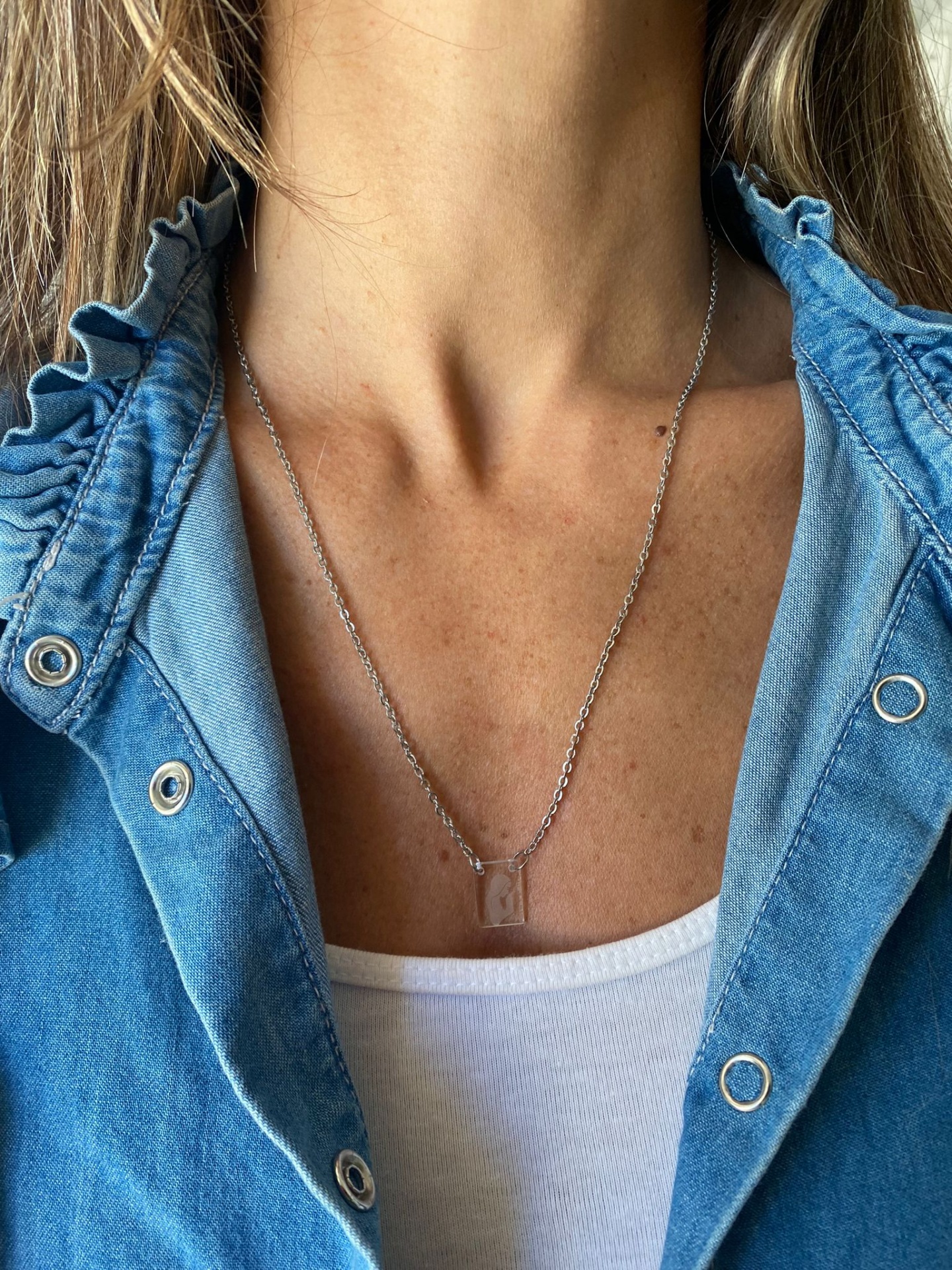 Colar prateado com pendente transparente retangular numa pessoa com camisa de ganga azul