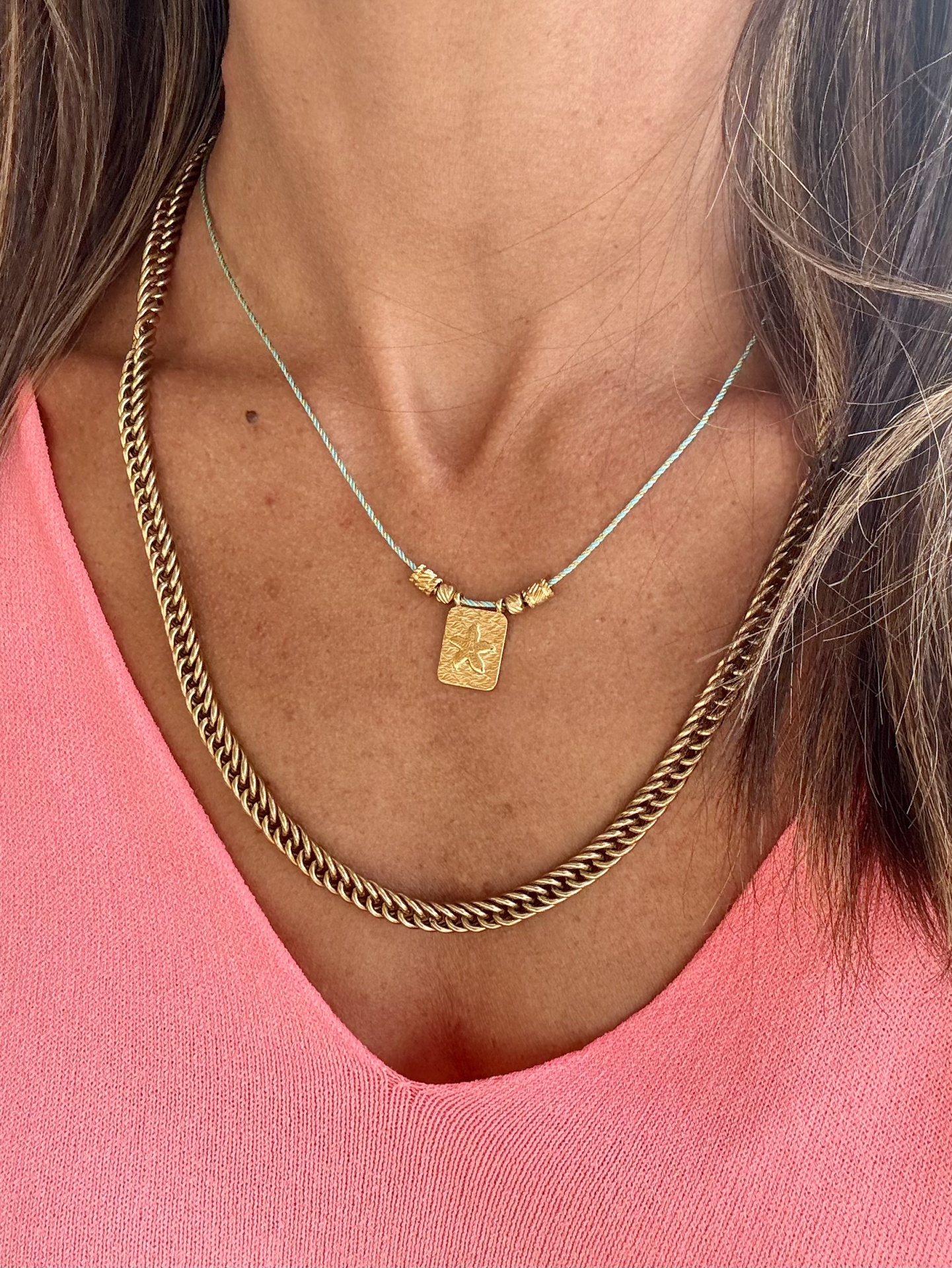 Duas colares dourados e azul claro usados por cima de blusa rosa