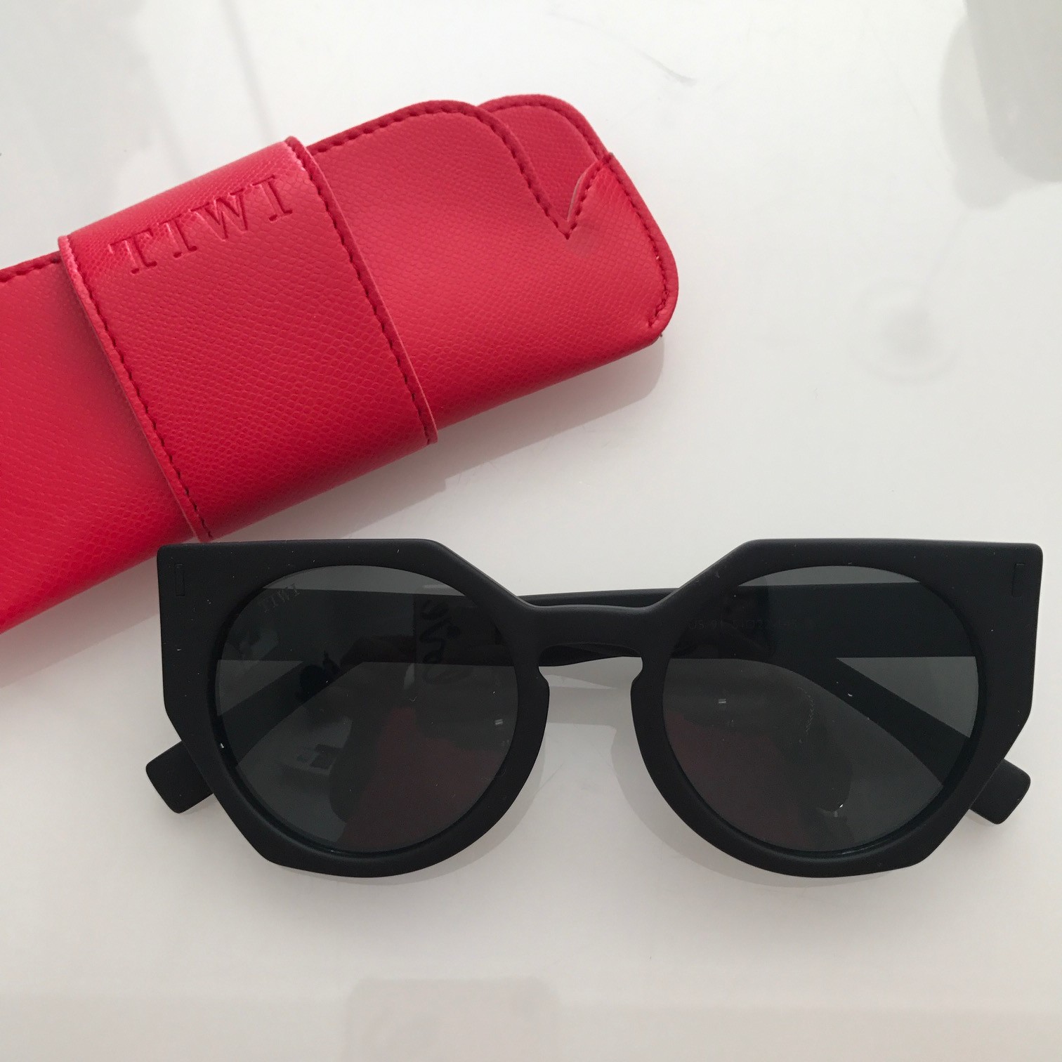 Óculos de sol pretos com bolsa vermelha de couro e texto TTIWI