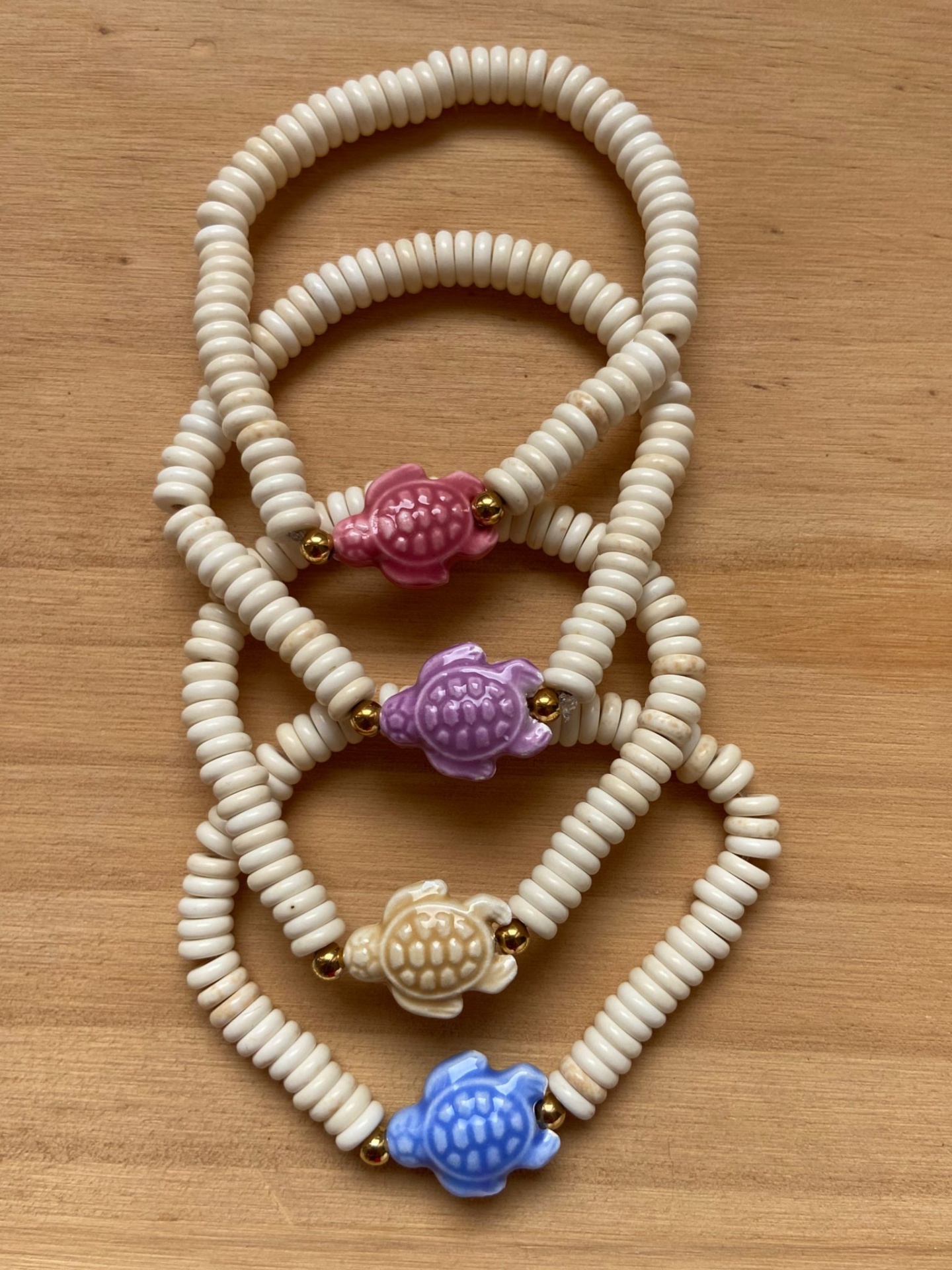 Pulseiras brancas com contas em forma de tartarugas coloridas sobre mesa de madeira.