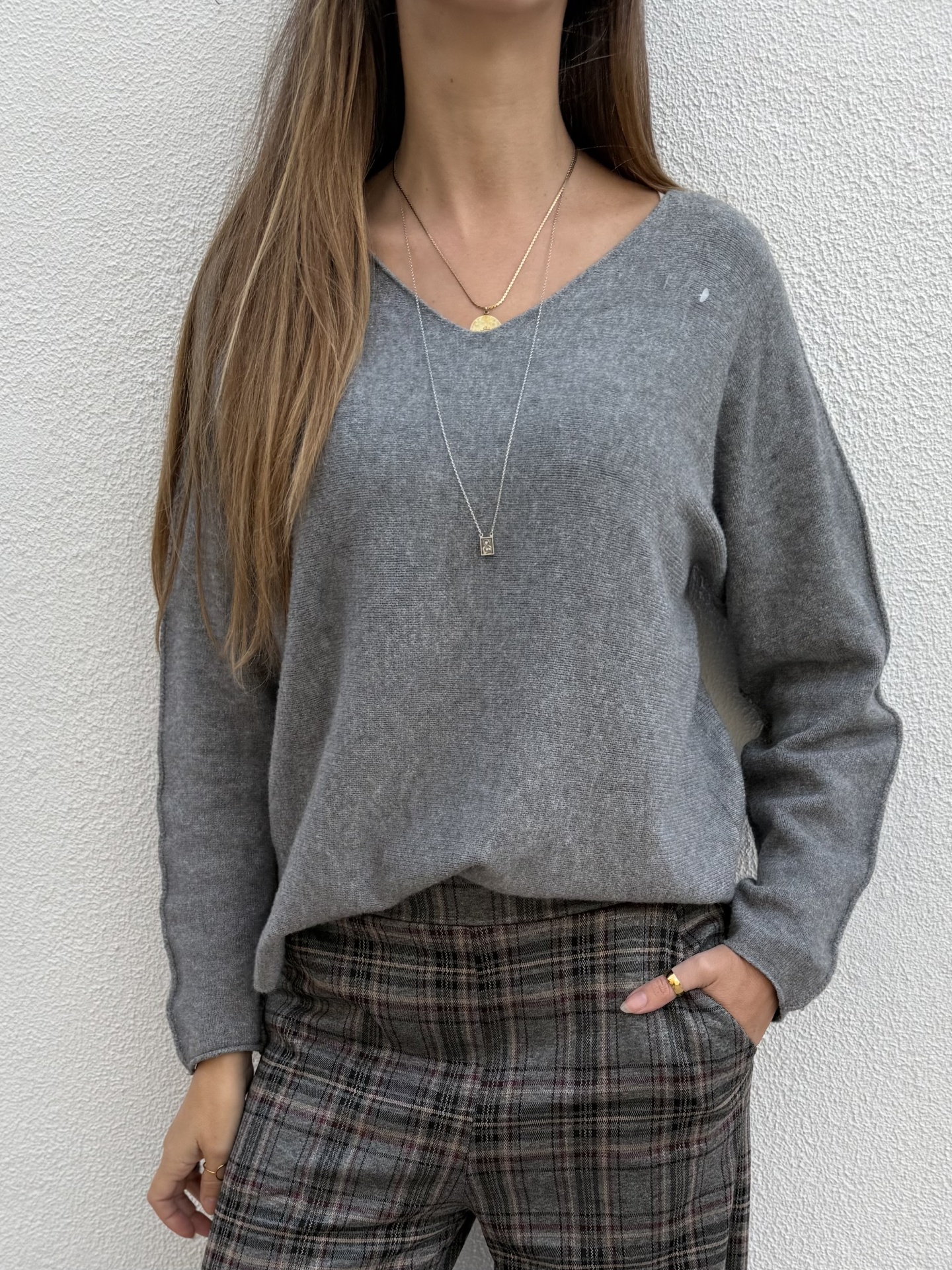 Mulher com camisola cinza de malha e calças de padrão xadrez num fundo branco