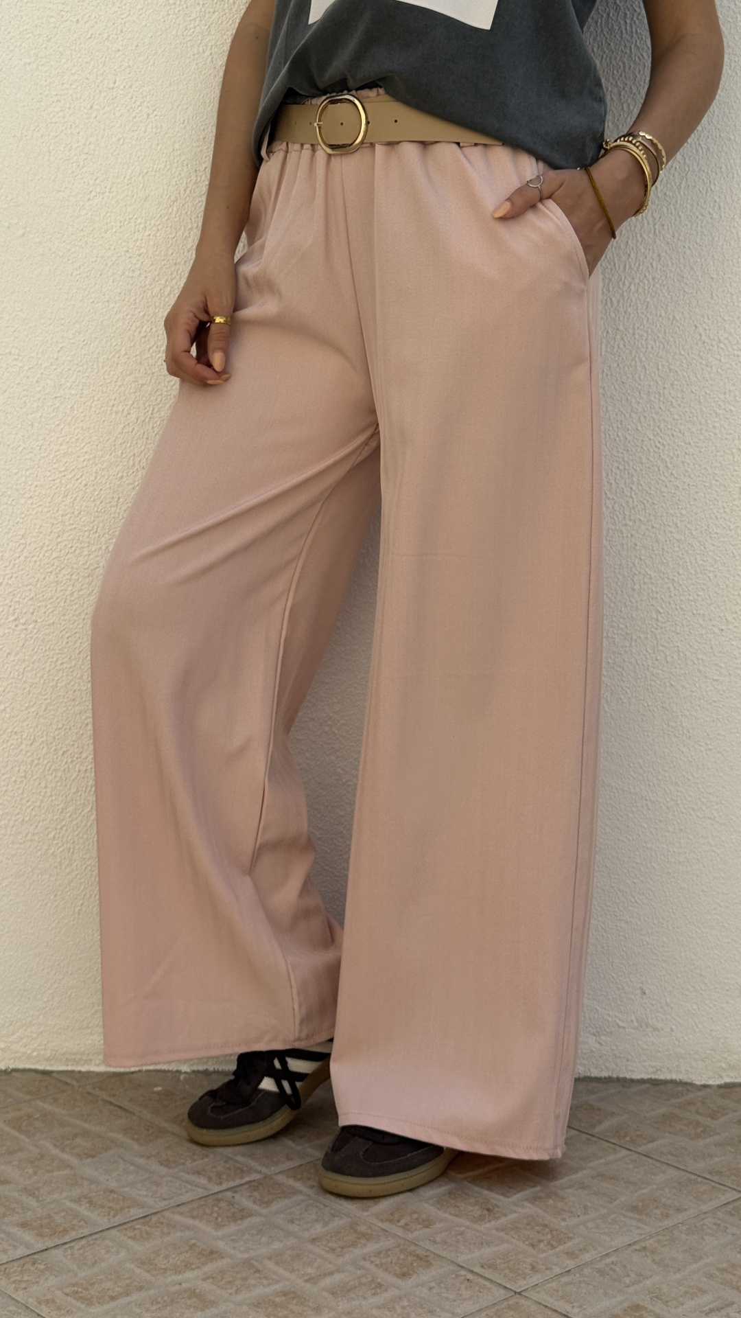 Calças largas rosa claro com cinto bege e sapatilhas castanhas num chão de azulejo