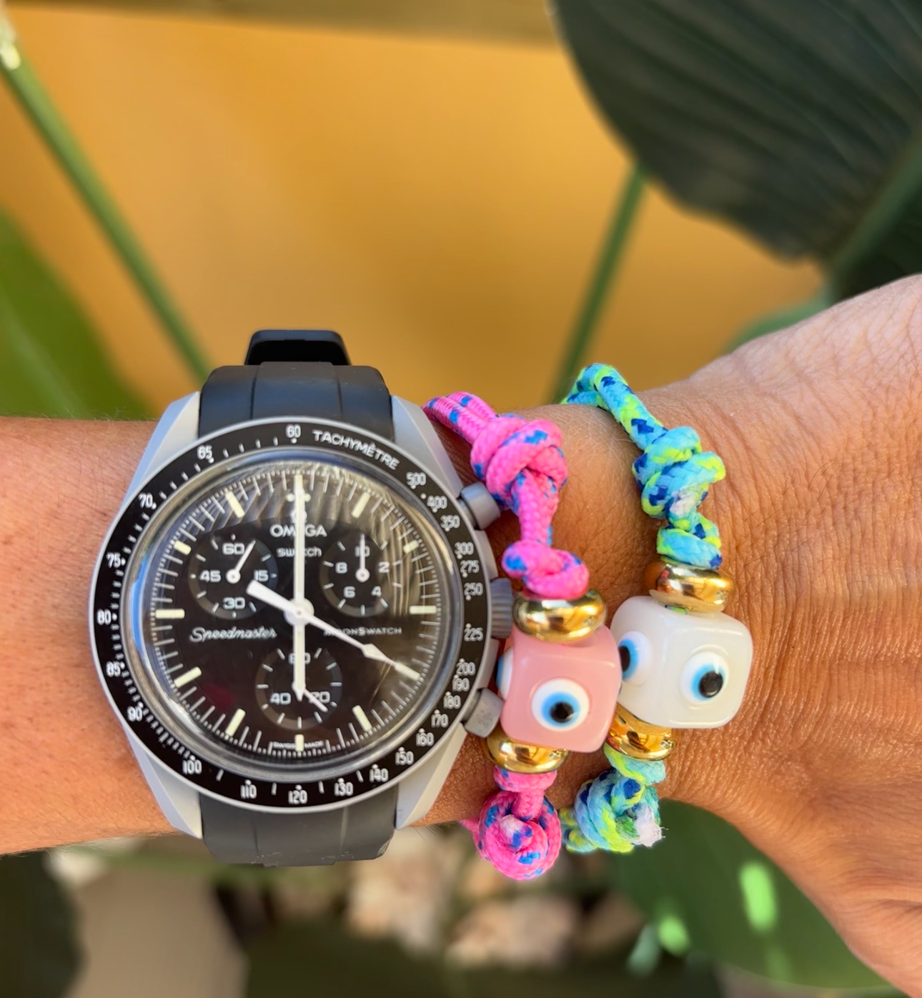 Relógio Omega Speedmaster preto com duas pulseiras coloridas de fio trançado e contas de olhos