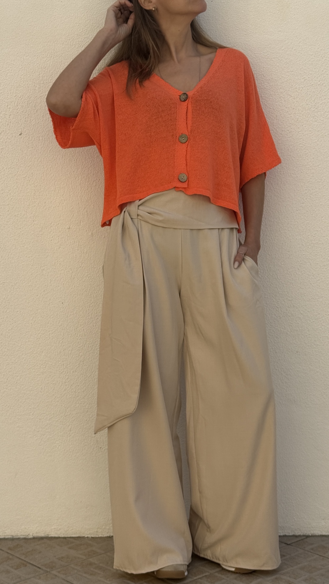 Top laranja de malha com botões e calças largas bege com faixa