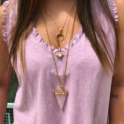 Colares dourados com pendentes de lua, estrela e pedra triangular em mulher com camisola rosa lilás