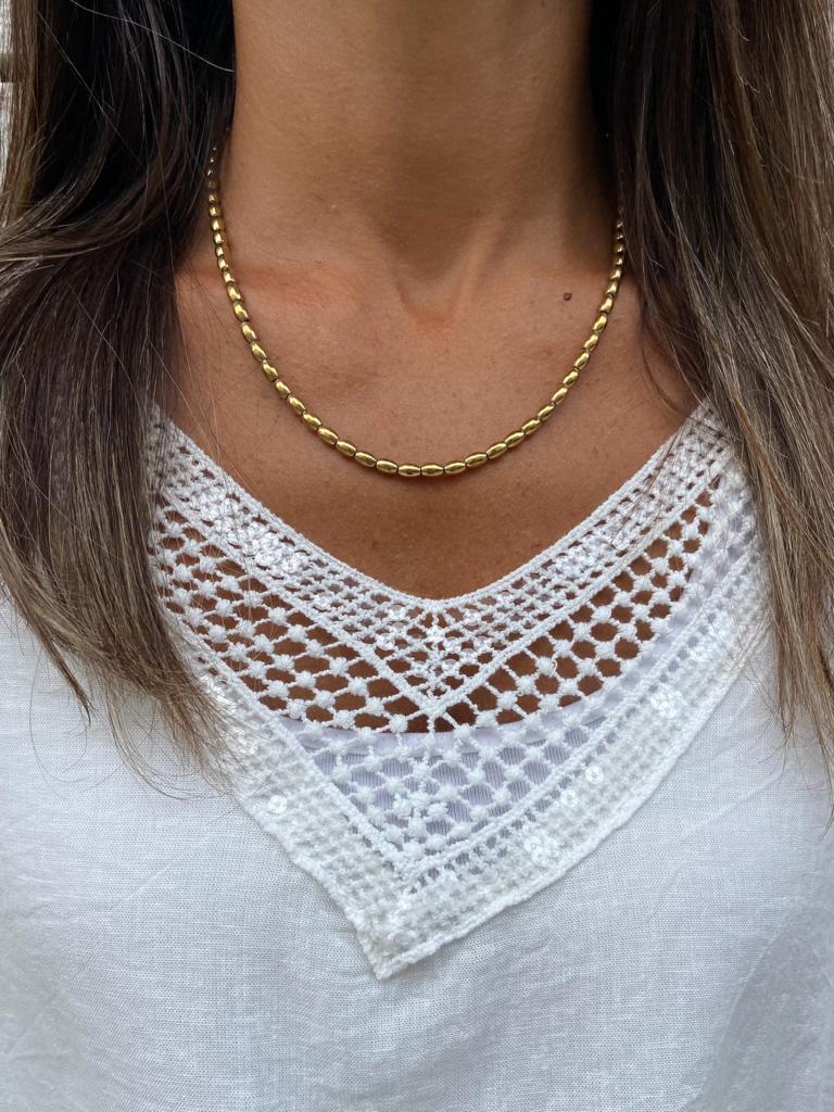 Colar dourado com contas e camisola branca com gola rendilhada em V