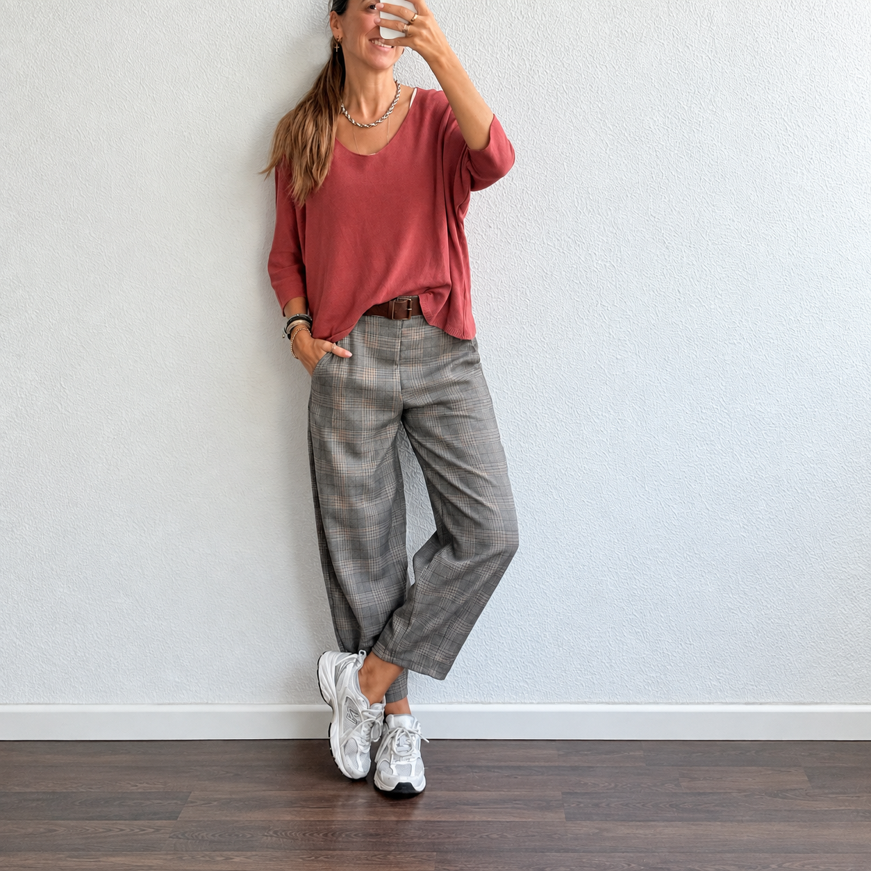 Pessoa com blusa terracota, calças xadrez cinzentas e sapatilhas brancas