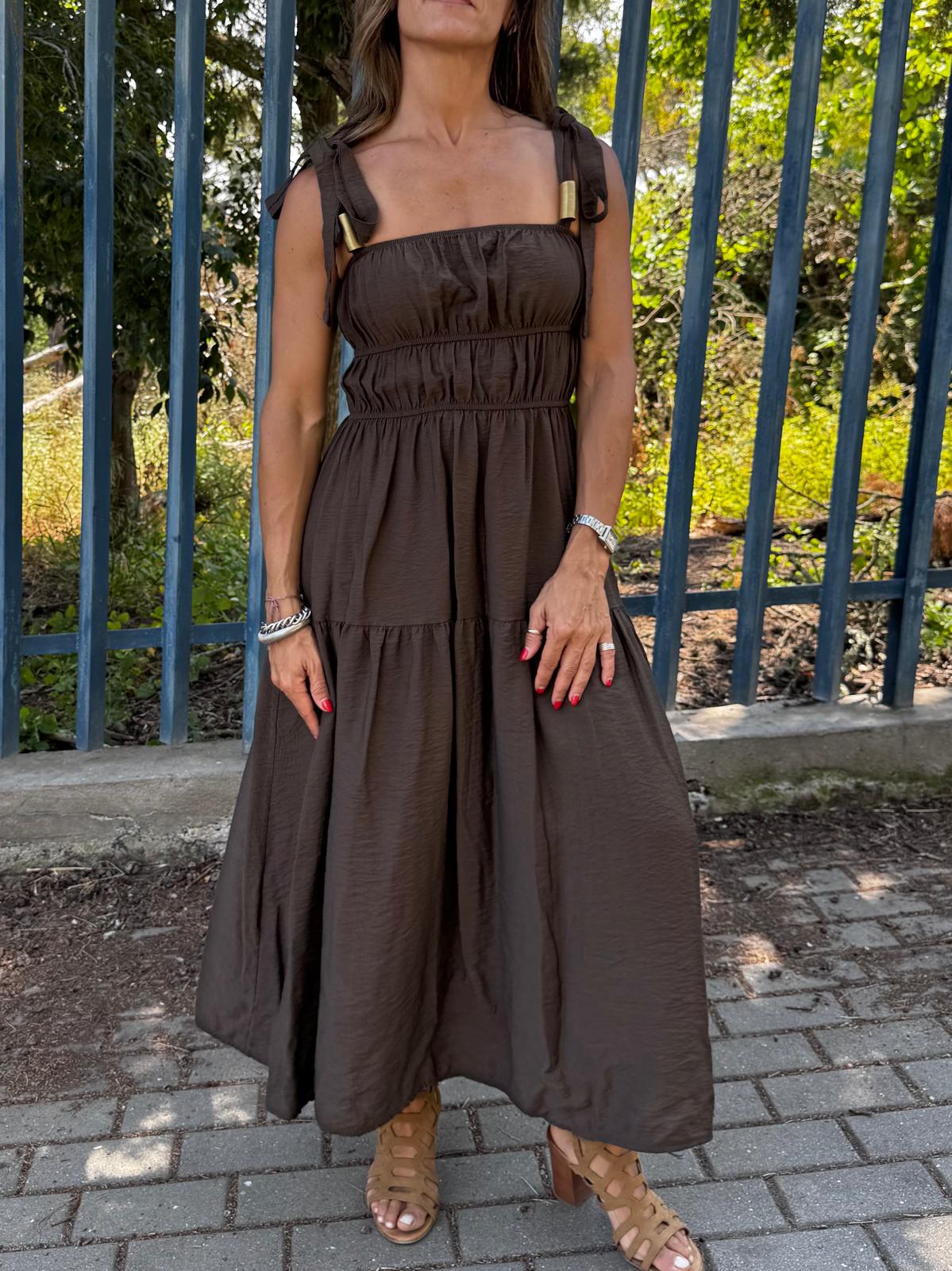 Vestido longo castanho com alças largas, tecido liso, usado com sandálias castanhas e pulseiras prateadas ao ar livre