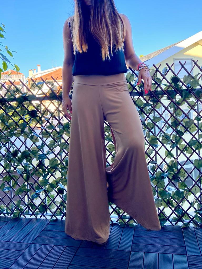 Calças largas castanho claro usadas por pessoa com top preto em varanda com treliça e plantas