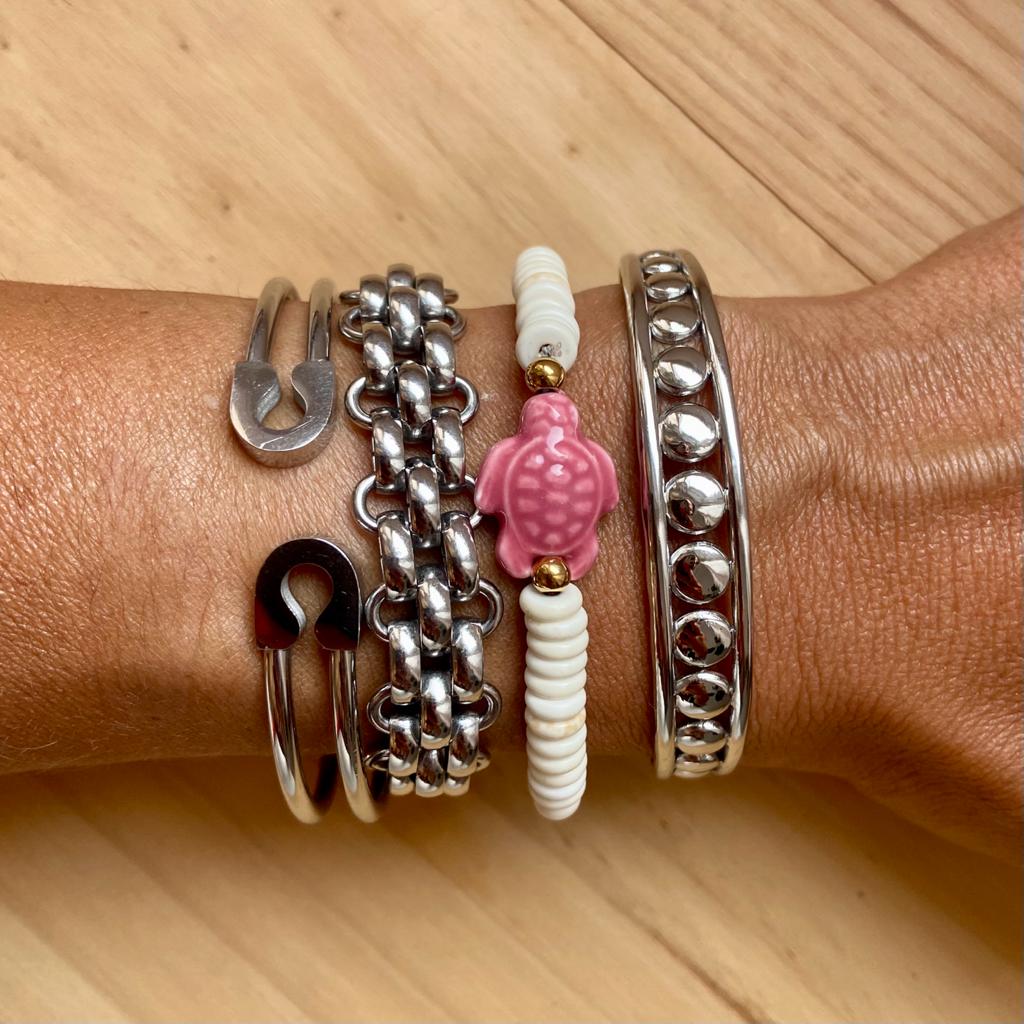 Mão com várias pulseiras metálicas e de contas sobre uma superfície de madeira clara