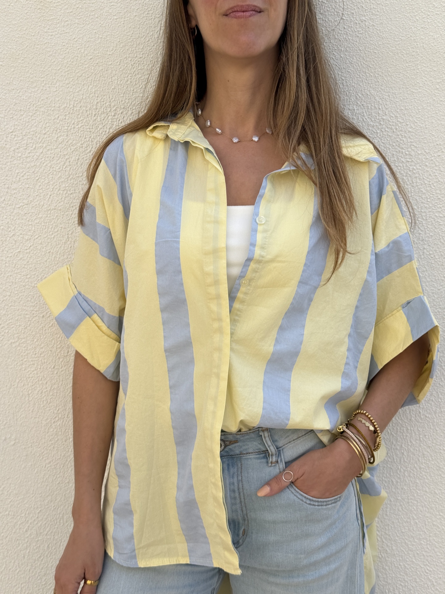 Camisa de riscas amarelas e azuis claras usada com jeans azuis e acessórios