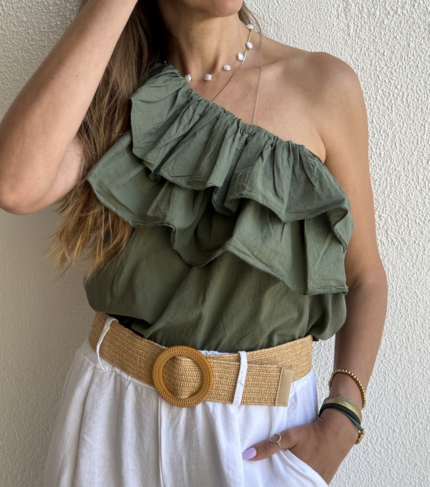 Top verde com folhos, calças brancas com cinto de fibra natural e acessórios coloridos