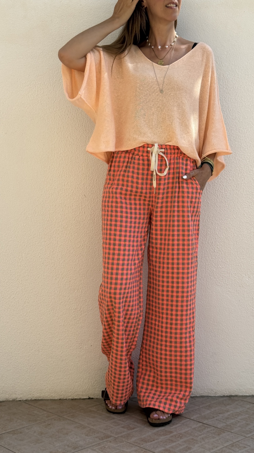 Mulher com blusa cor de pêssego e calças largas xadrez vermelho e castanho