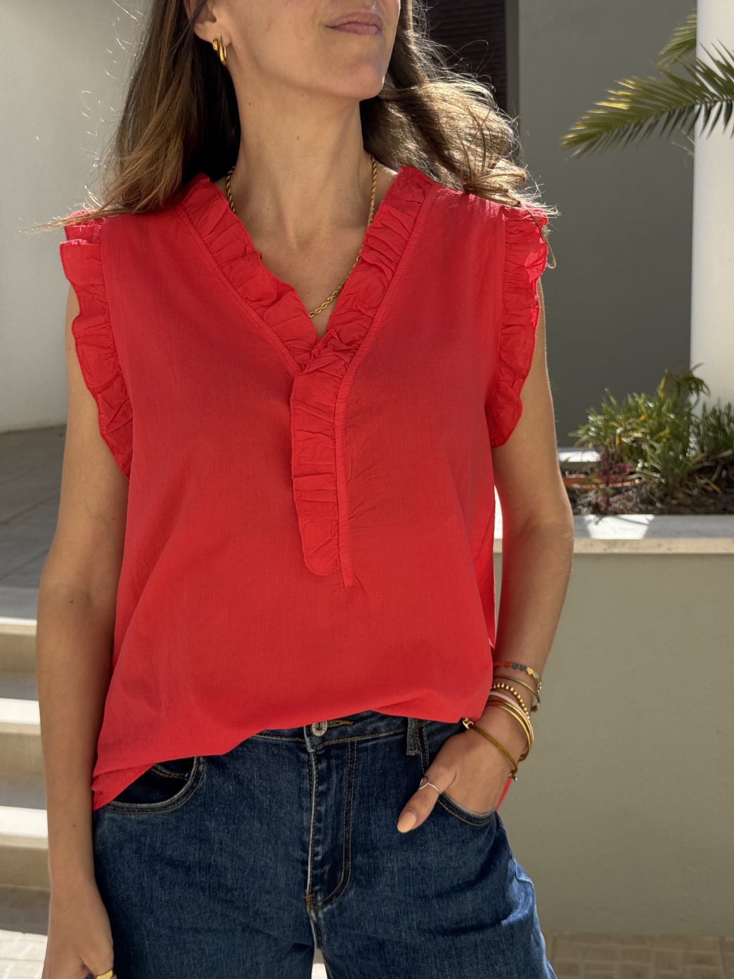 Blusa vermelha com folhos e calças de ganga azuis ao ar livre