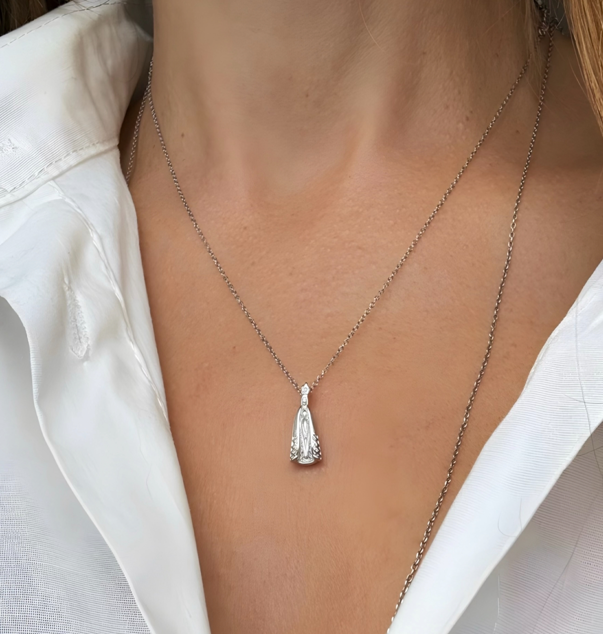 Colar prateado com pingente usado no pescoço com camisa branca.