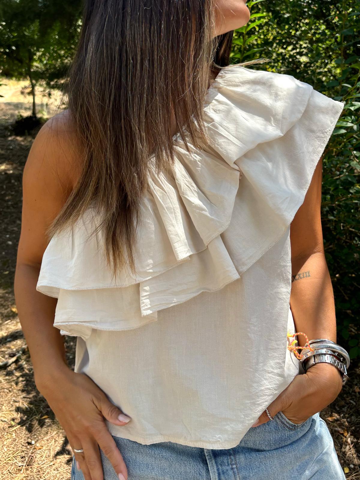 Blusa creme com babados assimétricos usada por mulher com calças jeans ao ar livre