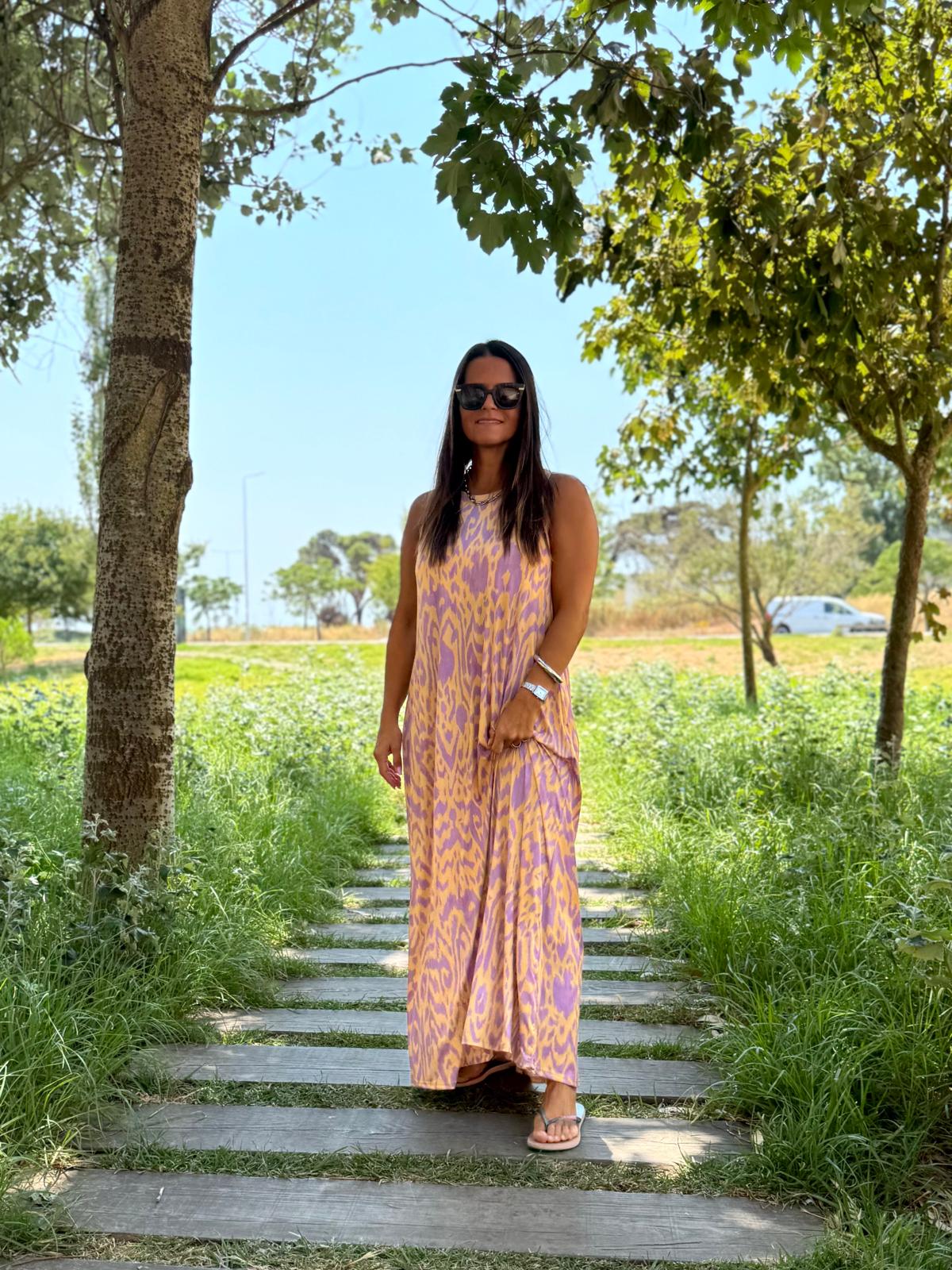 mulher com vestido comprido lilás e amarelo num caminho ao ar livre