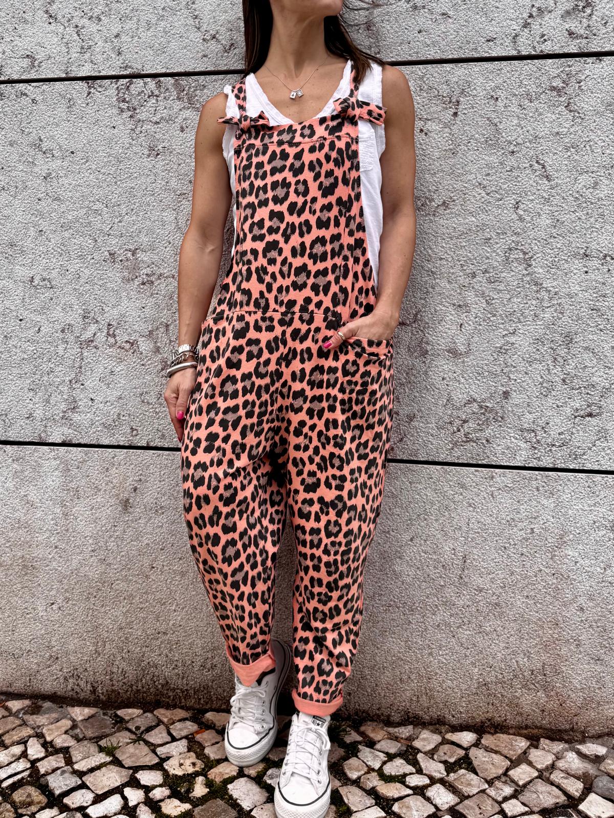 Macacão comprido feminino rosa com estampado animal, camiseta branca, sapatilhas, parede cinza de pedra