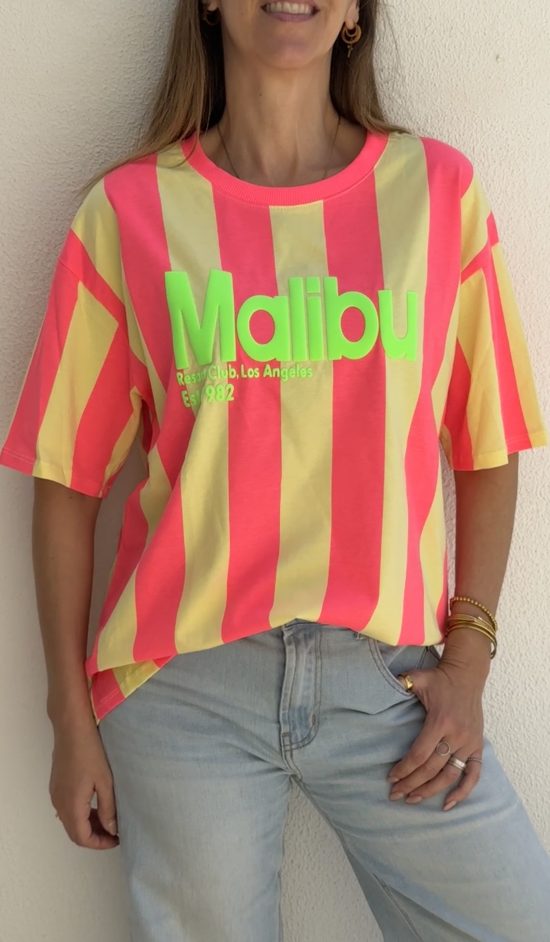 T-shirt riscada cor-de-rosa e amarelo com texto verde Malibu, combinada com jeans claros