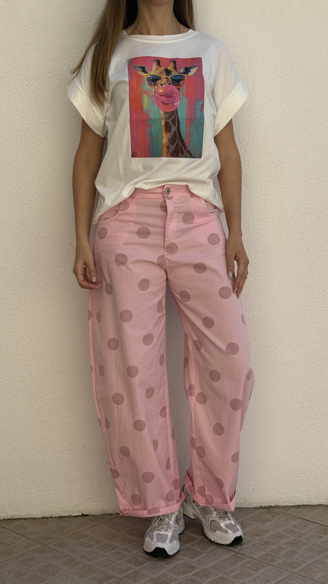 T-shirt branca com estampa de girafa colorida e calças rosa com bolinhas.