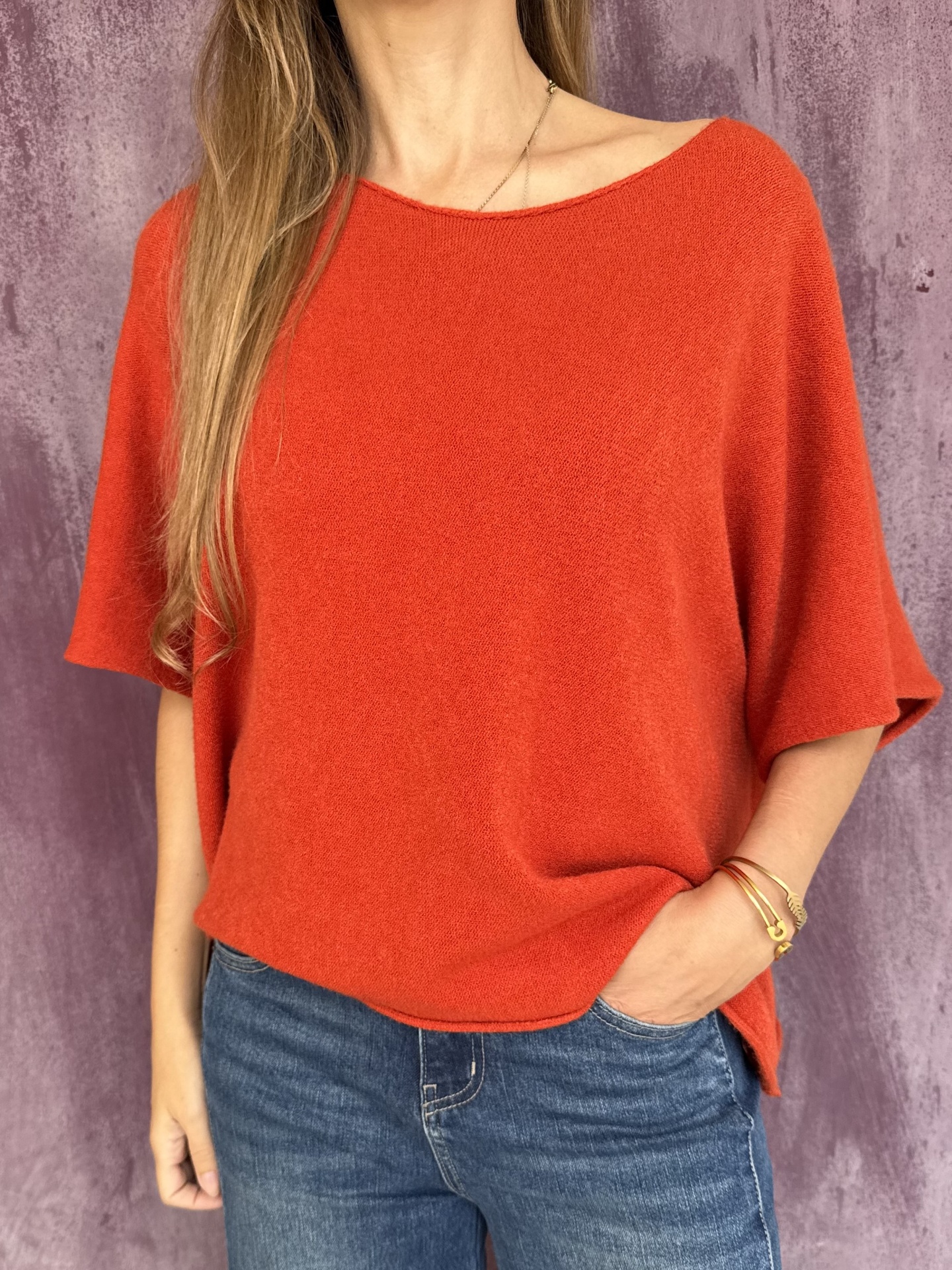 Camisola laranja de malha de manga curta com calças de ganga azuis em fundo roxo