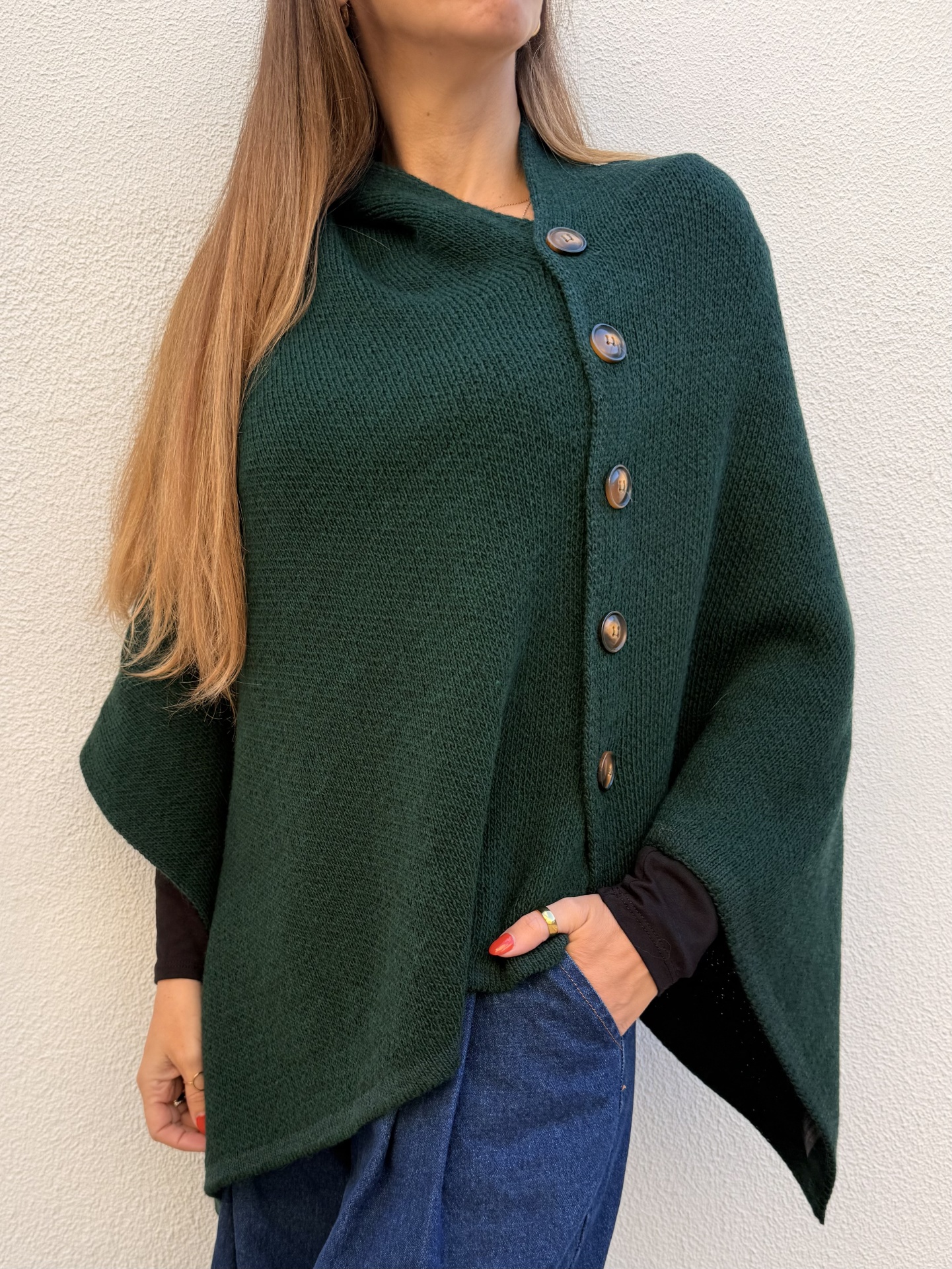 Poncho verde escuro de malha com botões visível num fundo branco