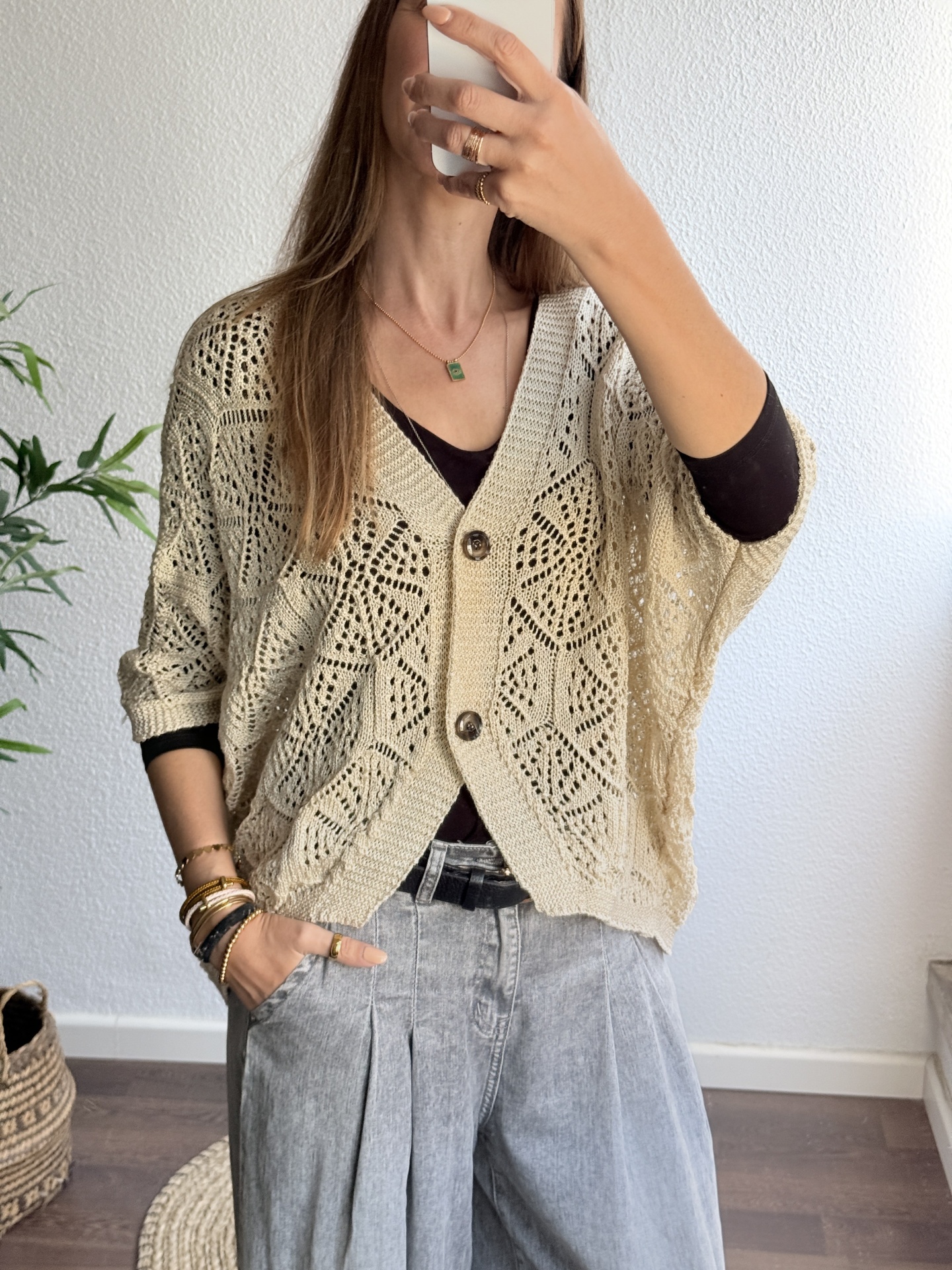 Cardigan bege com padrão rendado e botões, calças cinza e camisola preta, foto interior.