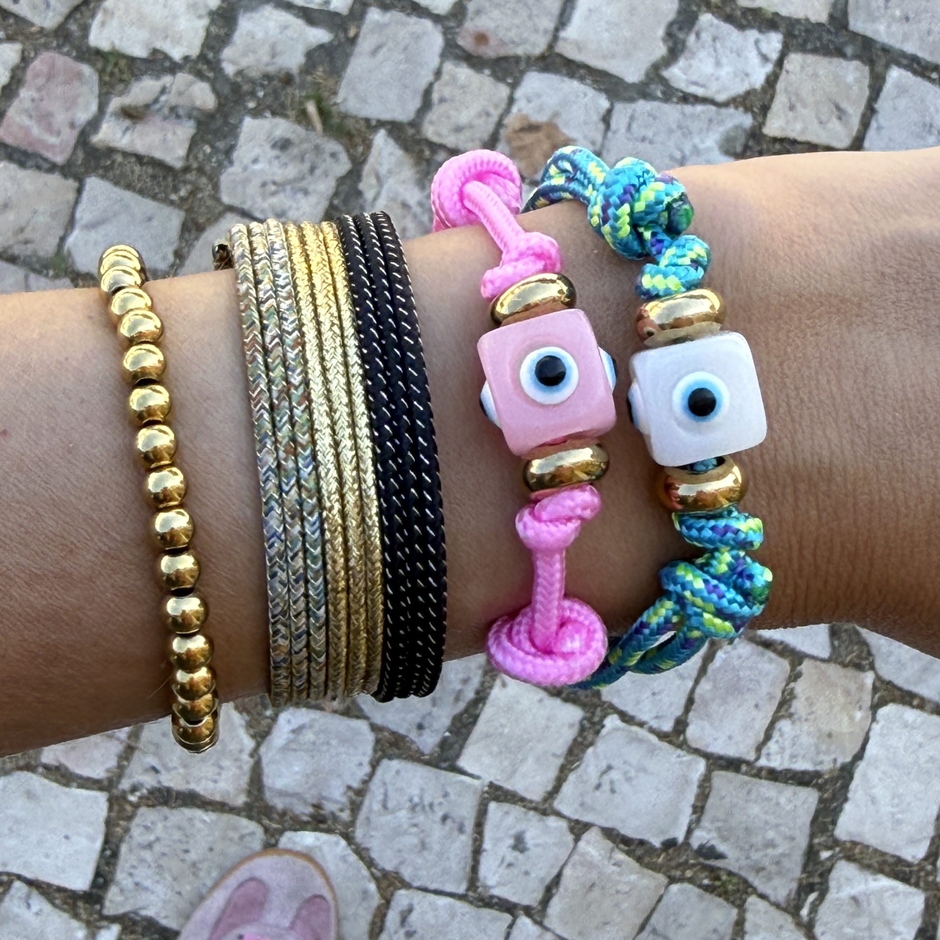 Pulseiras coloridas e metálicas num pulso sobre chão de calçada portuguesa.