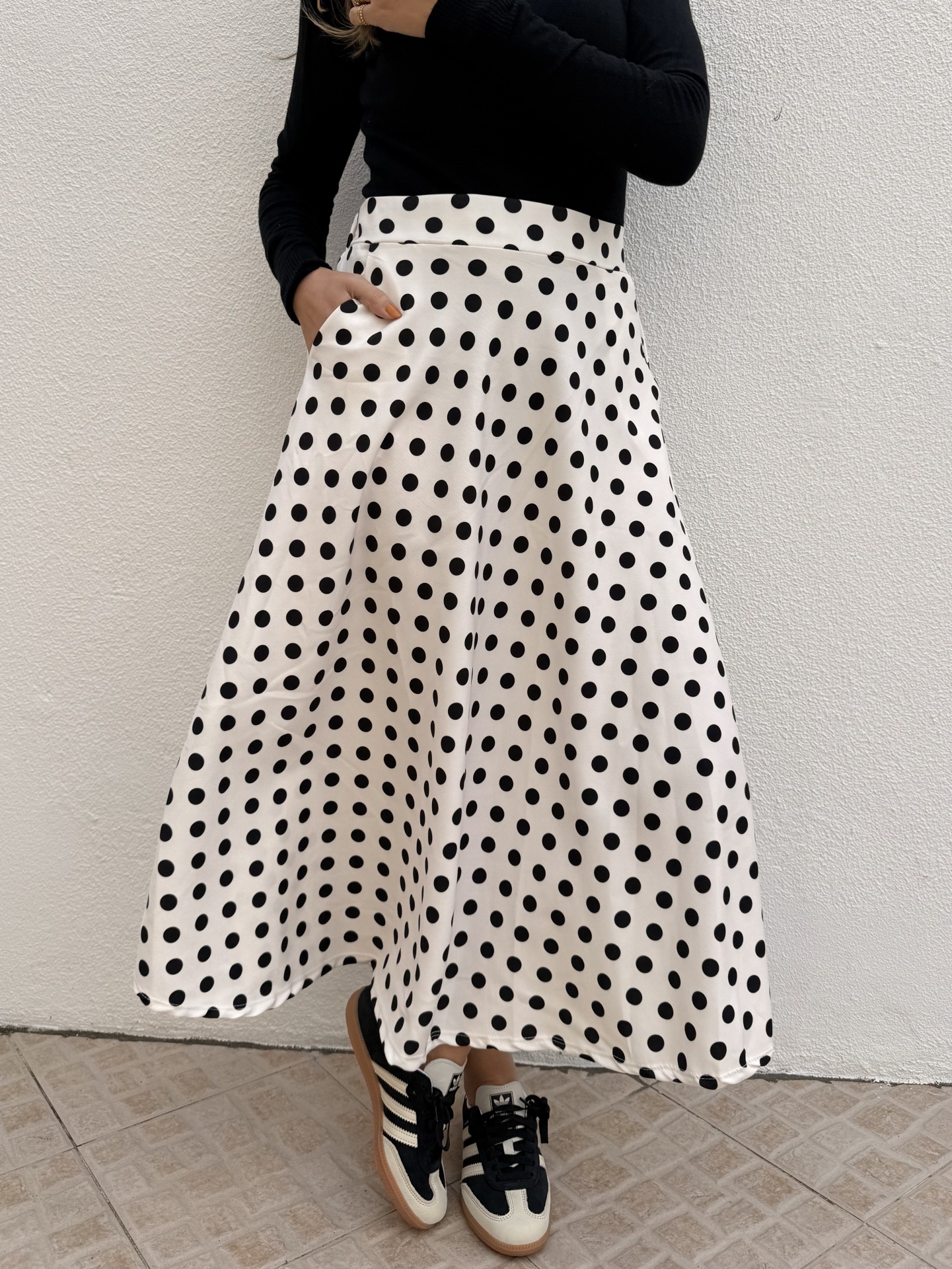 Saia midi branca com bolinhas pretas usada com camisola preta e ténis bicolores em fundo branco
