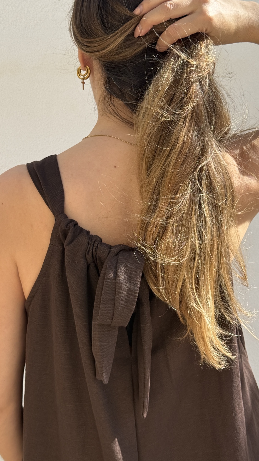 Pessoa de costas com vestido castanho e brincos dourados