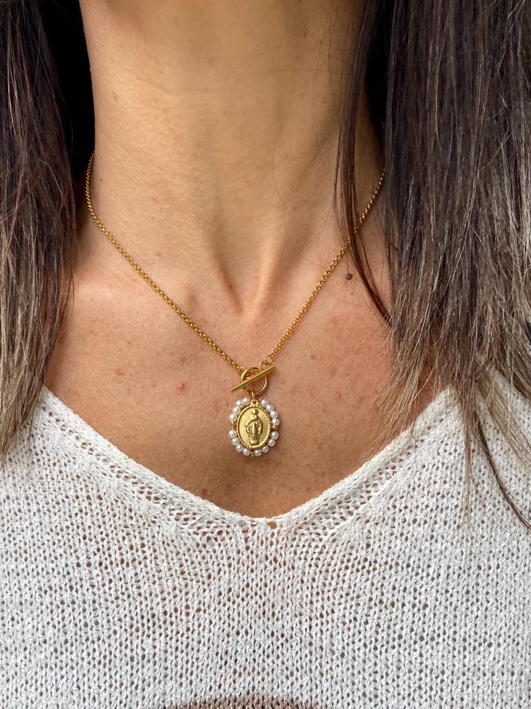 Colar dourado com pendente oval e pérolas numa camisola clara