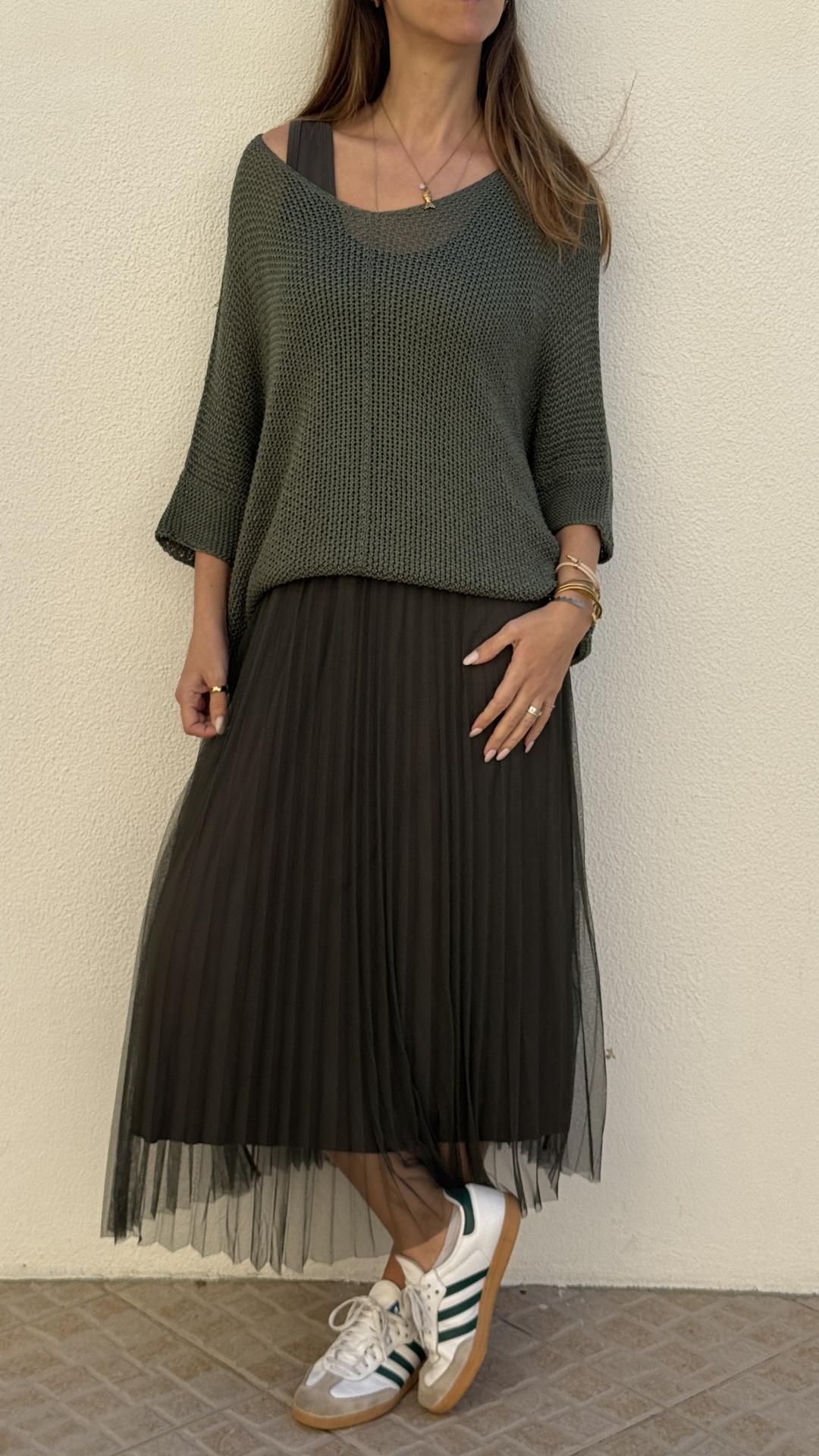 Mulher com camisola de malha verde e saia plissada preta com ténis brancos e riscas verdes