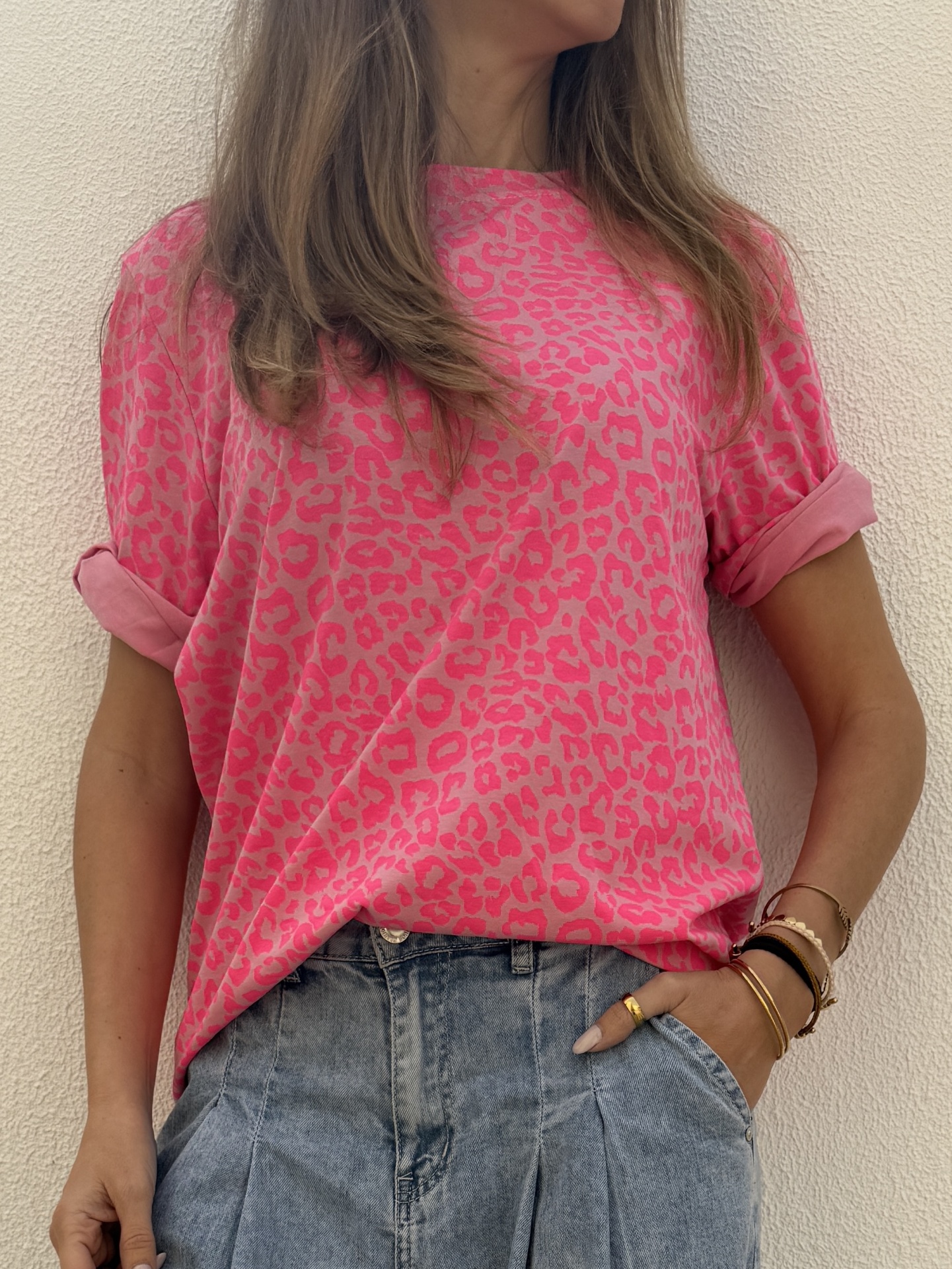 Pessoa com t-shirt rosa de padrão animal print e calças de ganga azul claro.