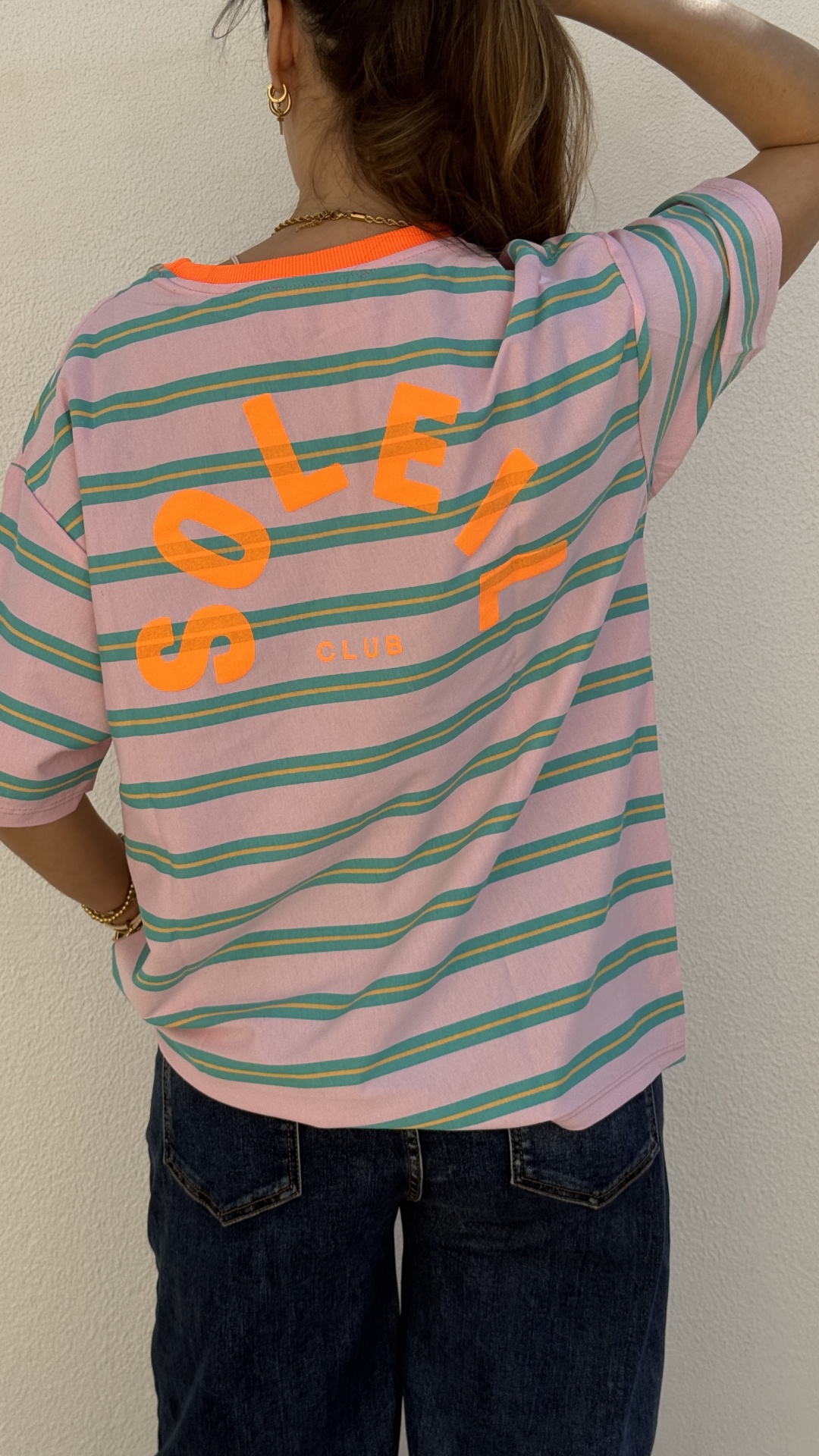 T-shirt riscada lilás com verde e amarelo e texto alaranjado nas costas